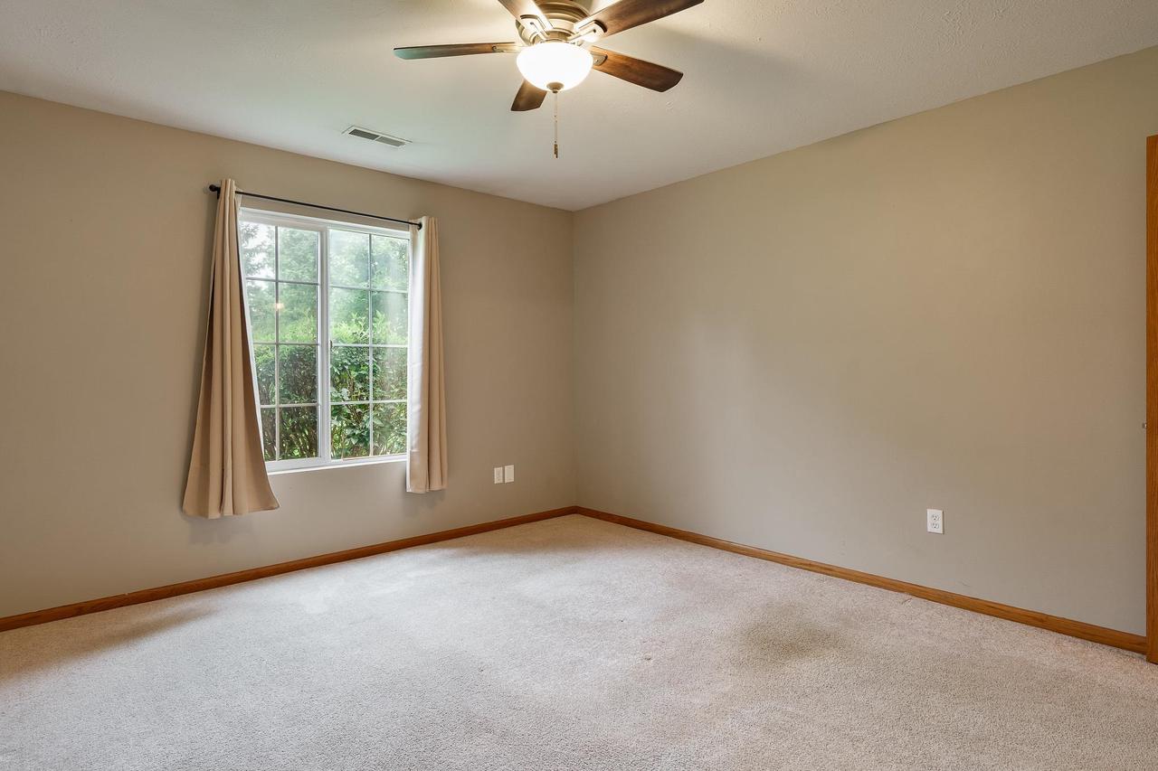 Empty bedroom with beige carpet, a curtained window, and a ceiling fan with light.
