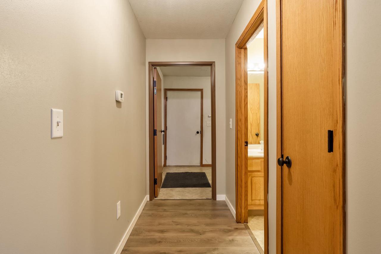 Hallway with wood-look flooring and oak-trimmed doors, with a bathroom vanity visible through an open doorway.