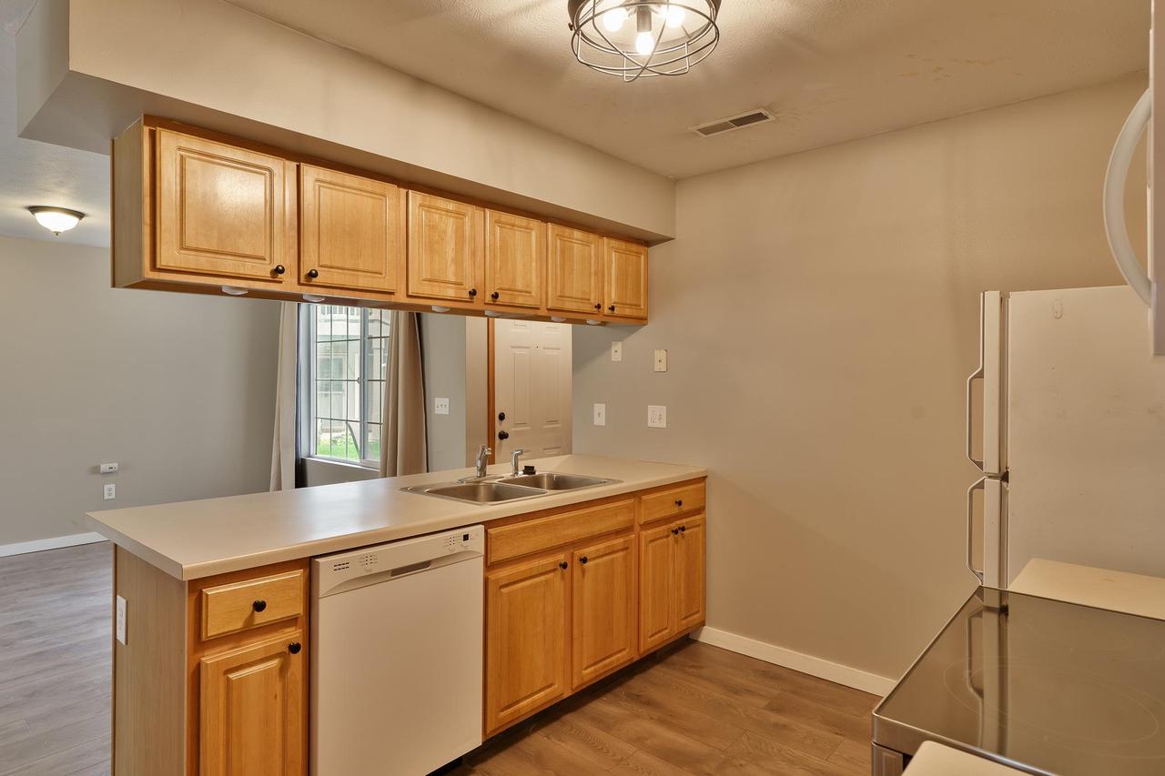 Kitchen with honey-colored wood cabinets, a double sink, dishwasher, and refrigerator.