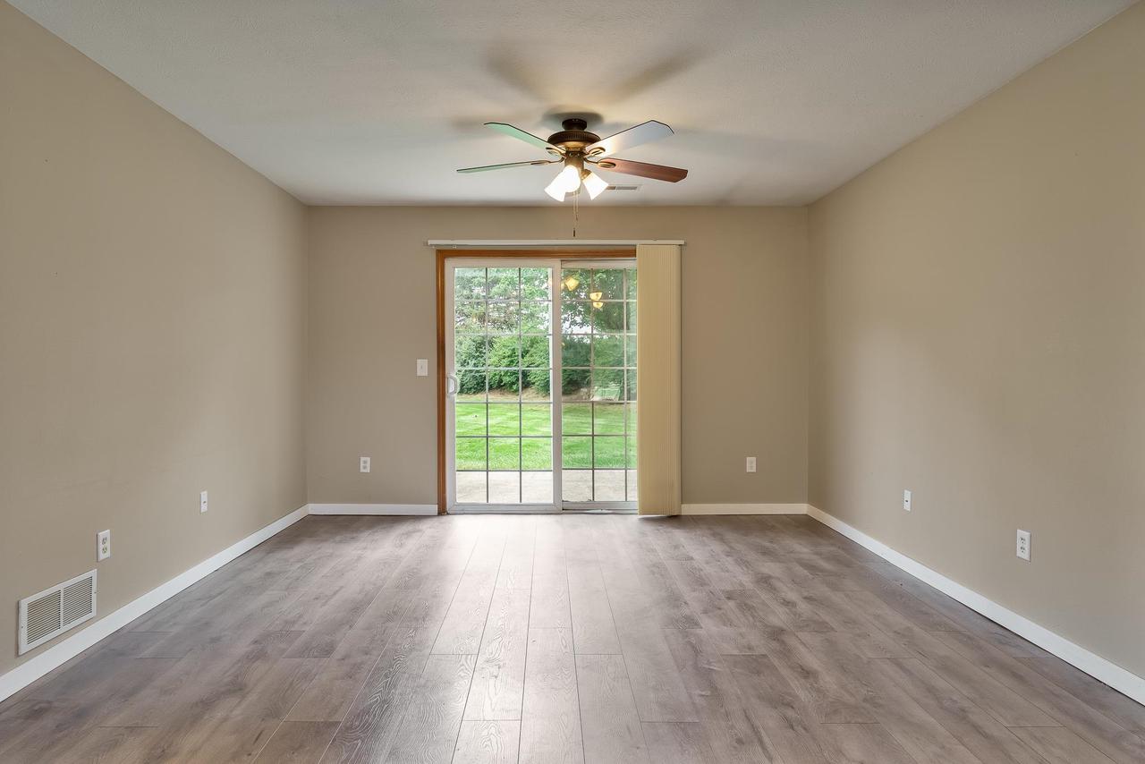 Empty living room with gray wood-look flooring, a ceiling fan, and sliding glass doors to the lawn.