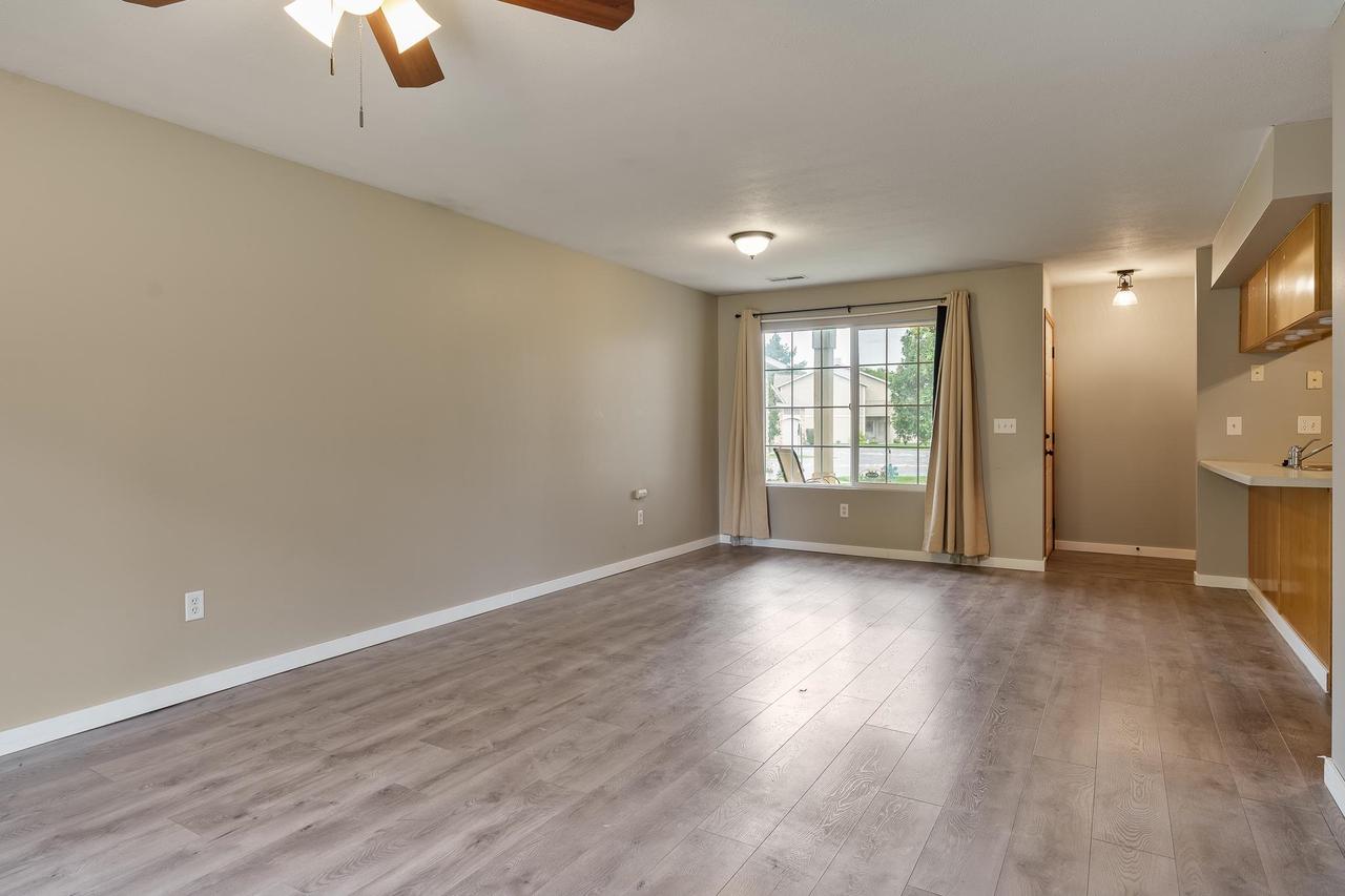 Vacant living room with gray wood-look flooring and a large curtained window.