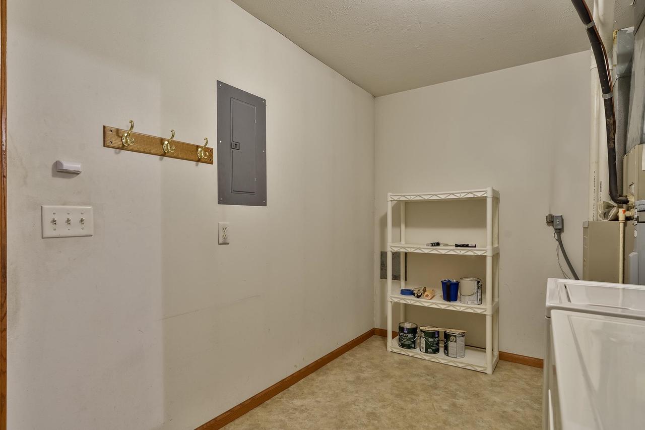 Utility room with a white wire storage shelf, paint cans, exposed pipes, and a sink or appliance.