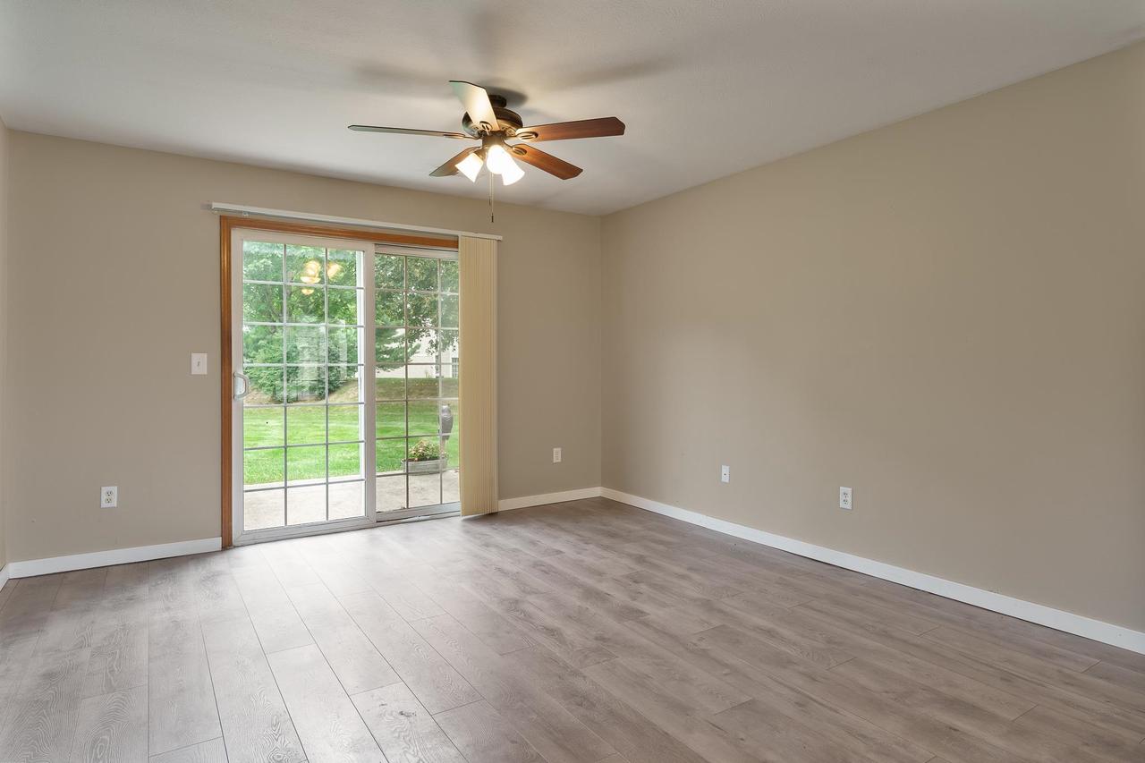 Empty room with wood-look flooring, ceiling fan, and sliding glass doors to the backyard.