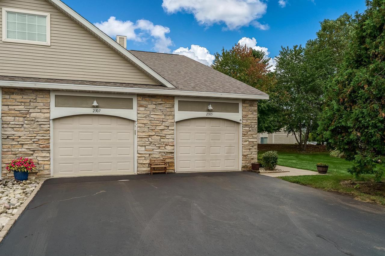 Front exterior with two stone-trimmed garages marked 2307 and 2305 beside a wide asphalt driveway.