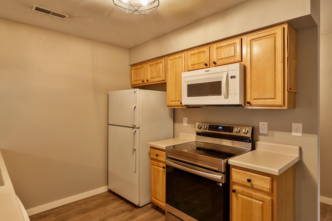 Kitchen with light wood cabinets, white refrigerator and microwave, and stainless-steel range.
