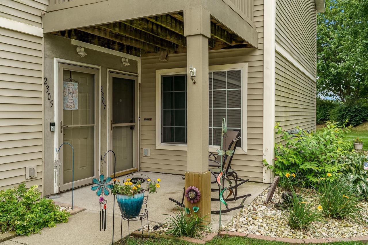 Covered entrance at 2307 Turnberry Court with patio chairs, potted flowers, and a rock garden.