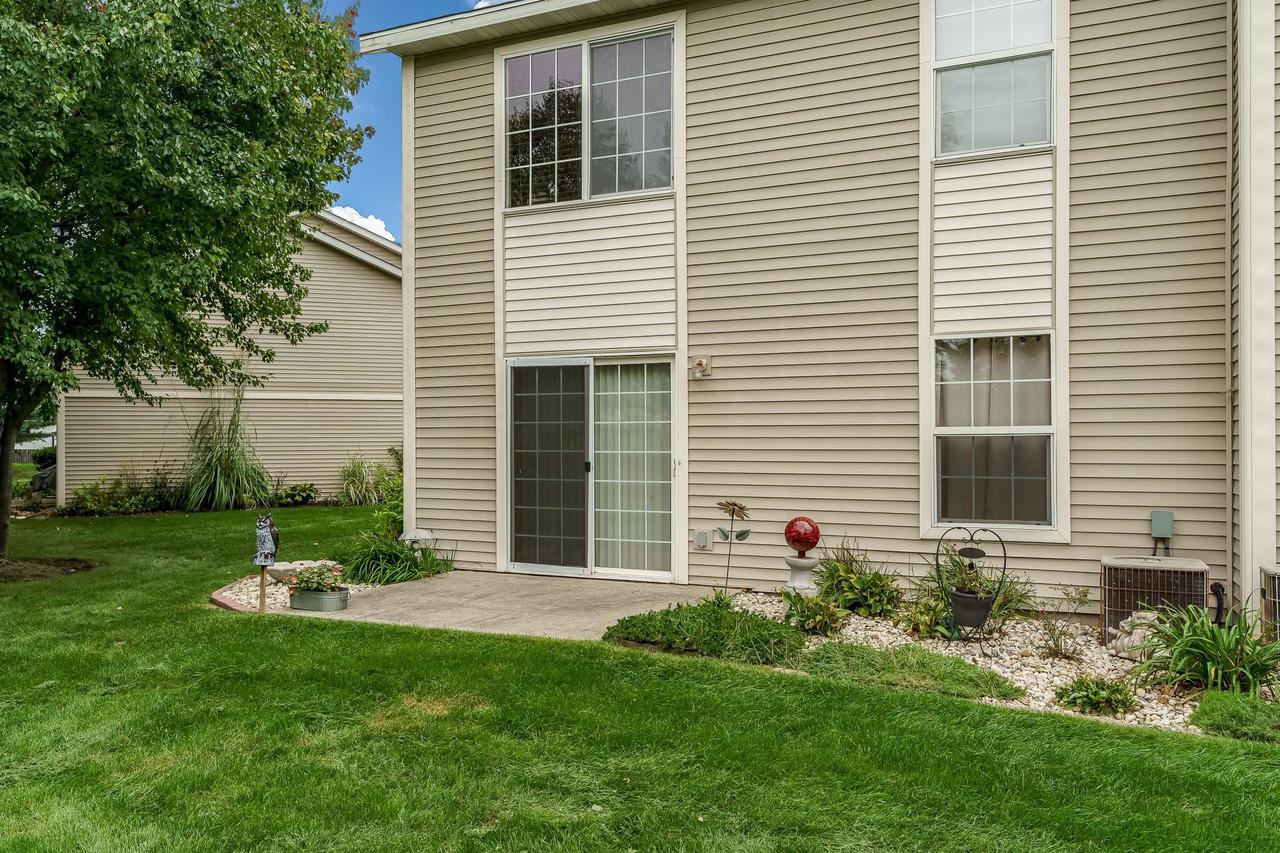 Rear of a beige two-story home with a patio door, lawn, and landscaped garden beds.