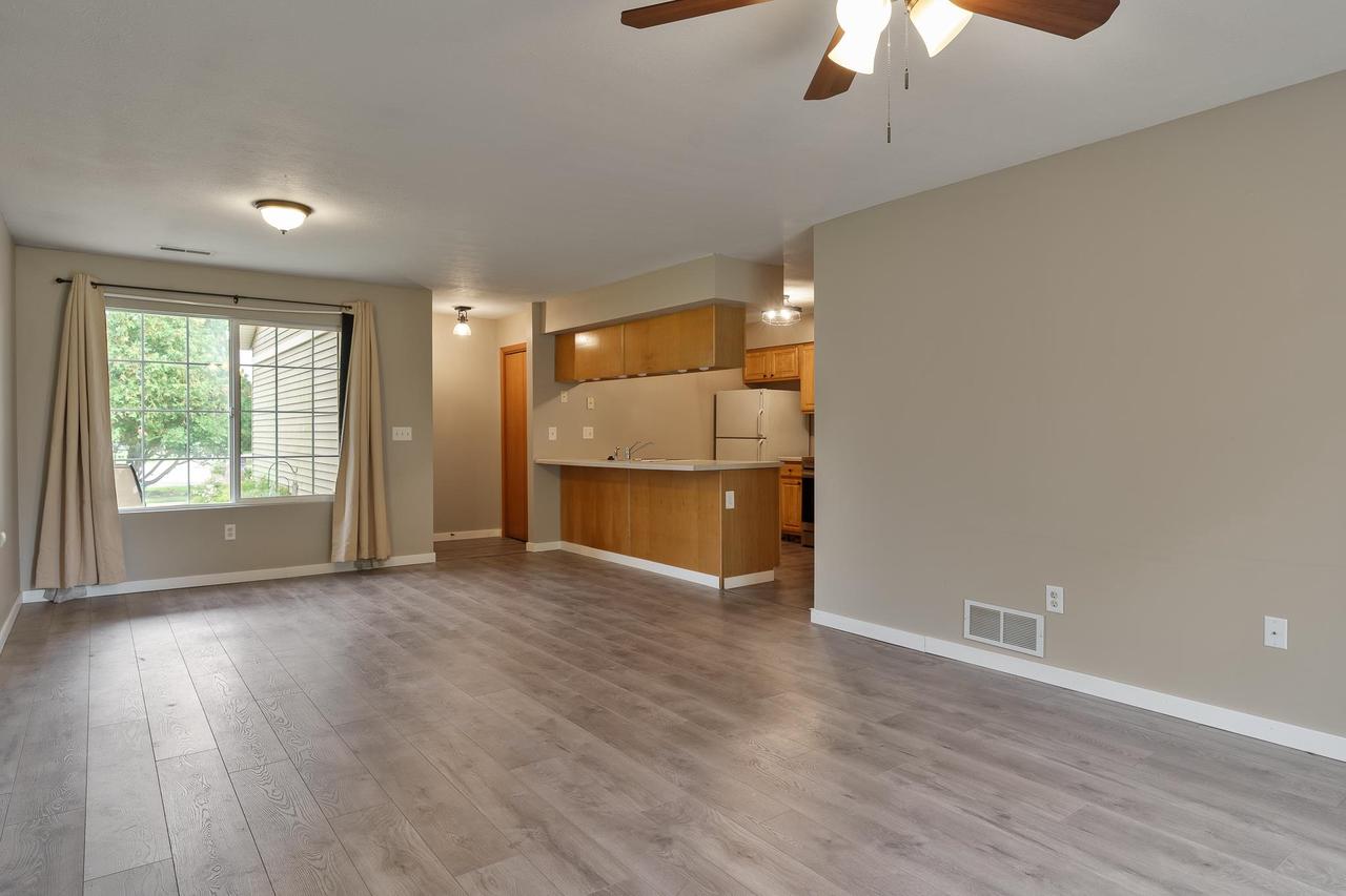Open-plan living area with plank flooring, a large curtained window, and an adjoining wood-cabinet kitchen.