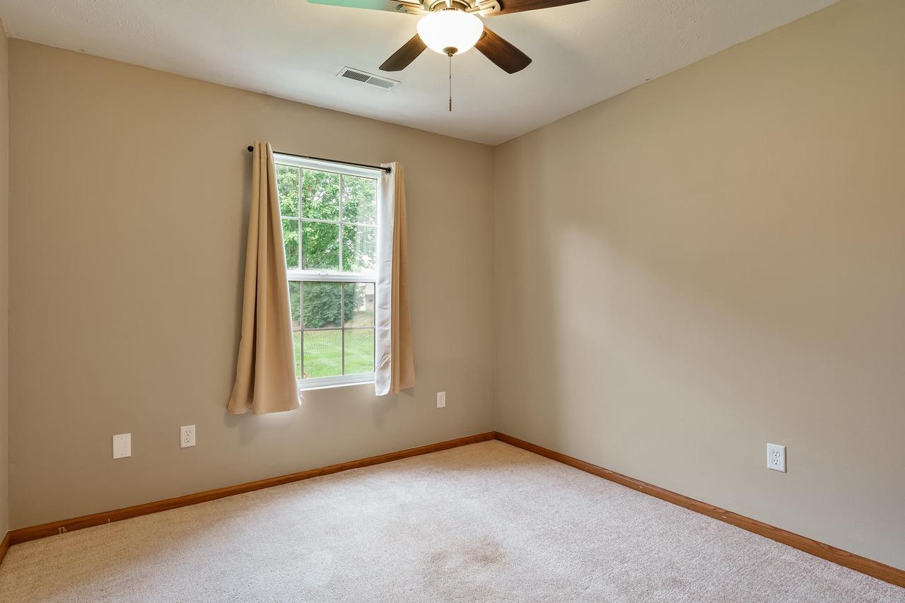 Empty carpeted bedroom with a curtained window and ceiling fan.