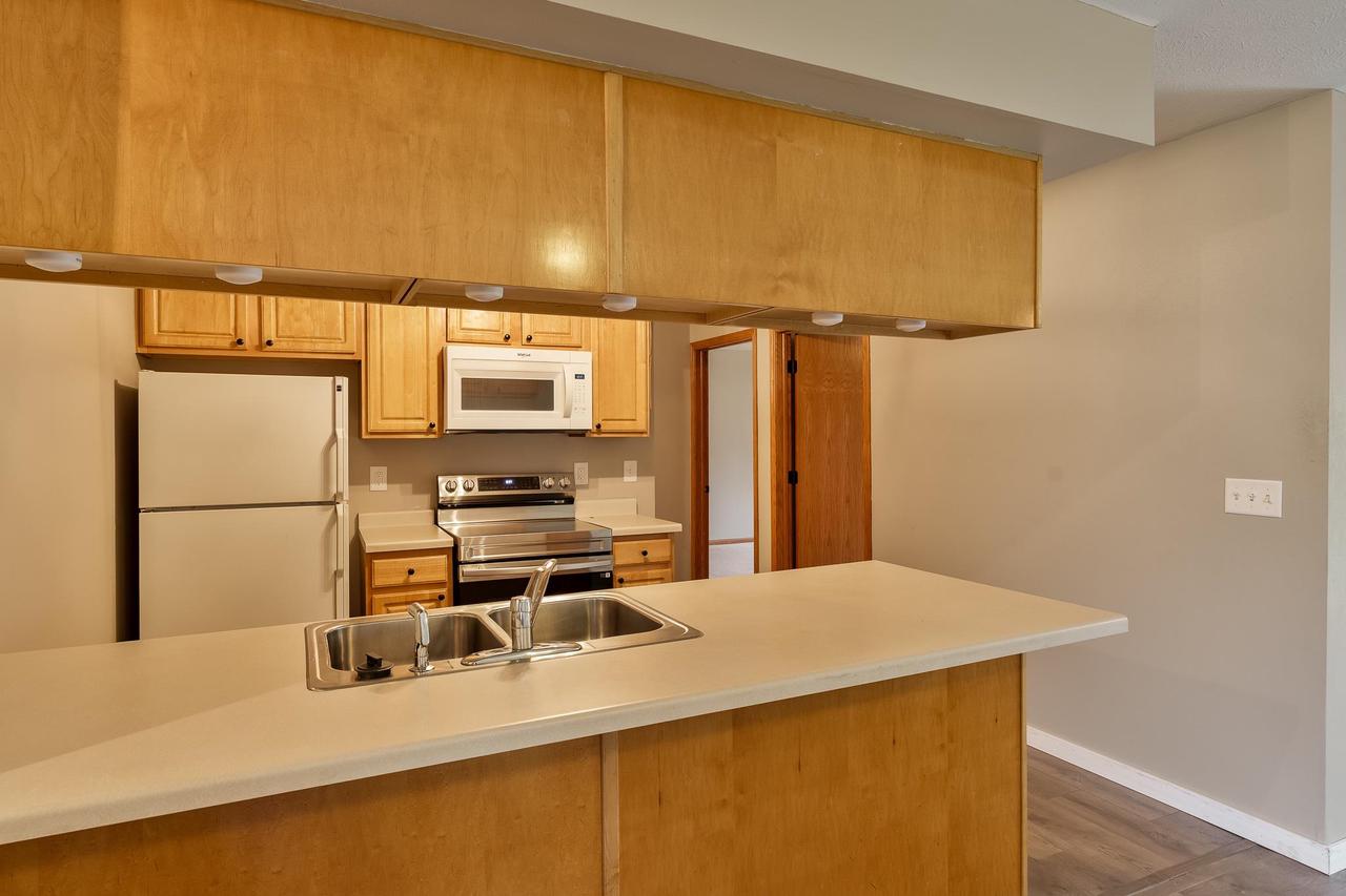 Kitchen with a large peninsula, double-basin sink, wood cabinetry, and stainless steel range.
