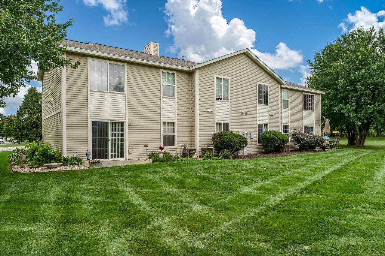 Rear of a beige two-story home with a sliding glass door overlooking a broad green lawn.