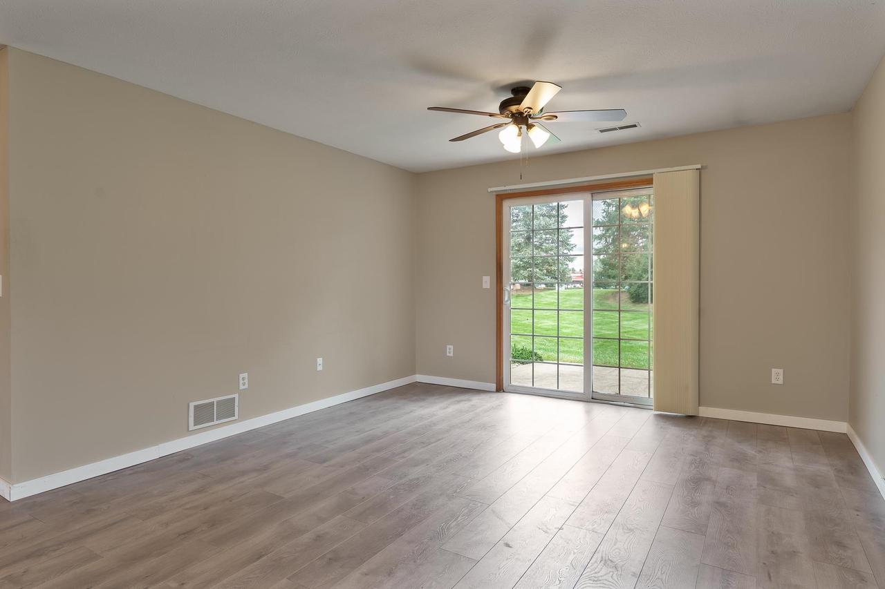Empty room with gray wood-look floors and a sliding glass door overlooking a green lawn.
