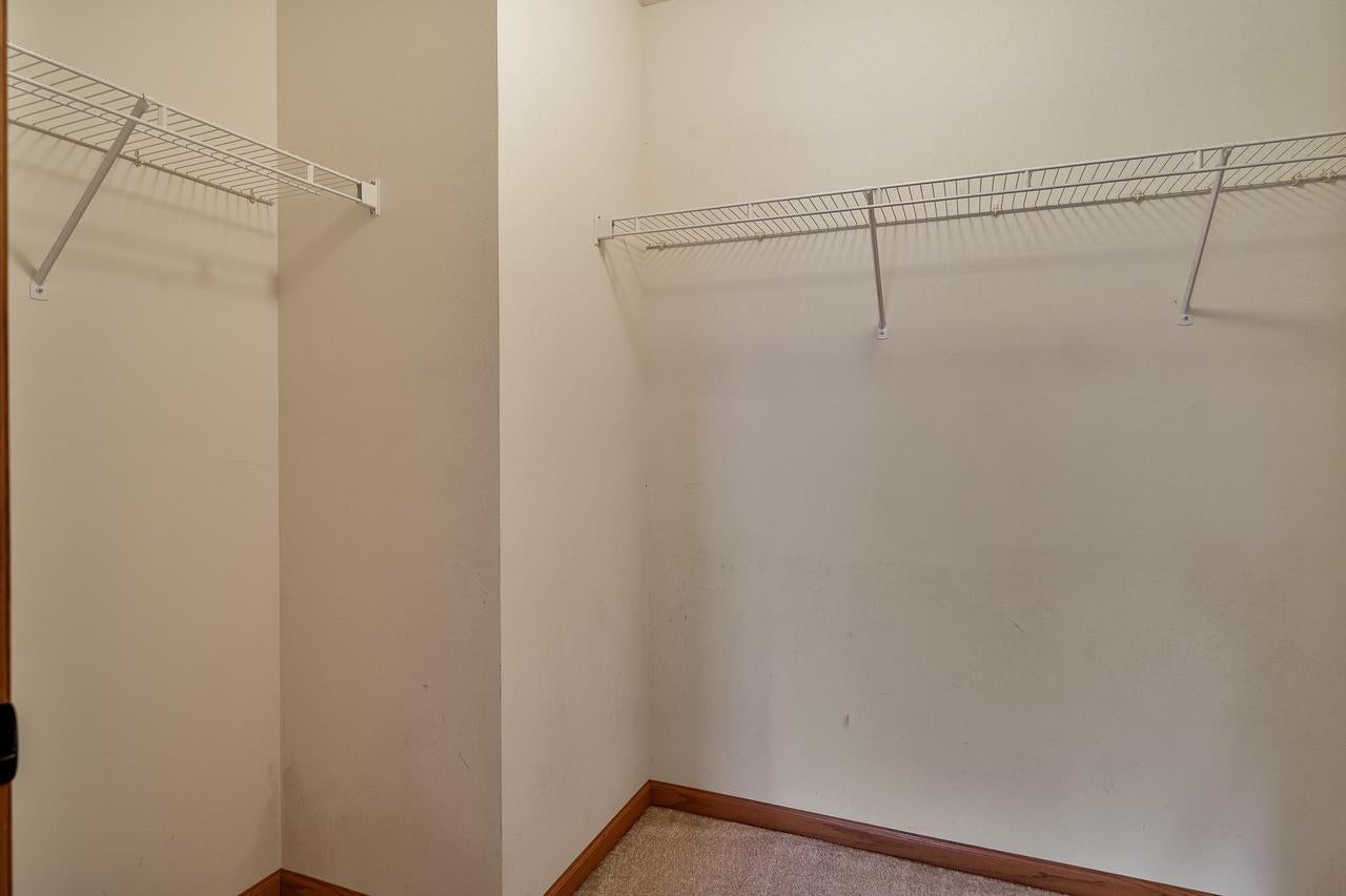 Empty walk-in closet with wire shelving on two walls and beige carpeting.