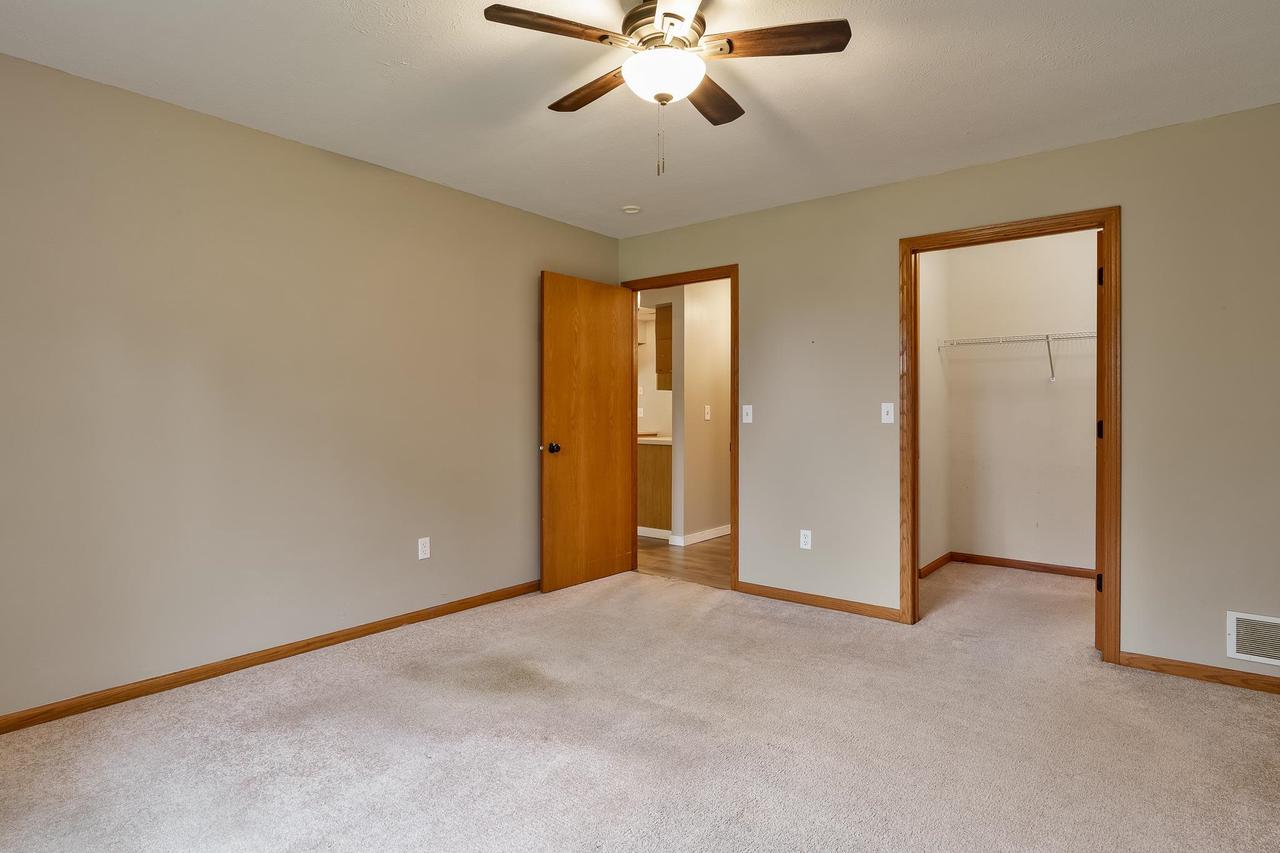 Empty carpeted bedroom with a ceiling fan, wood trim, and an open closet doorway.