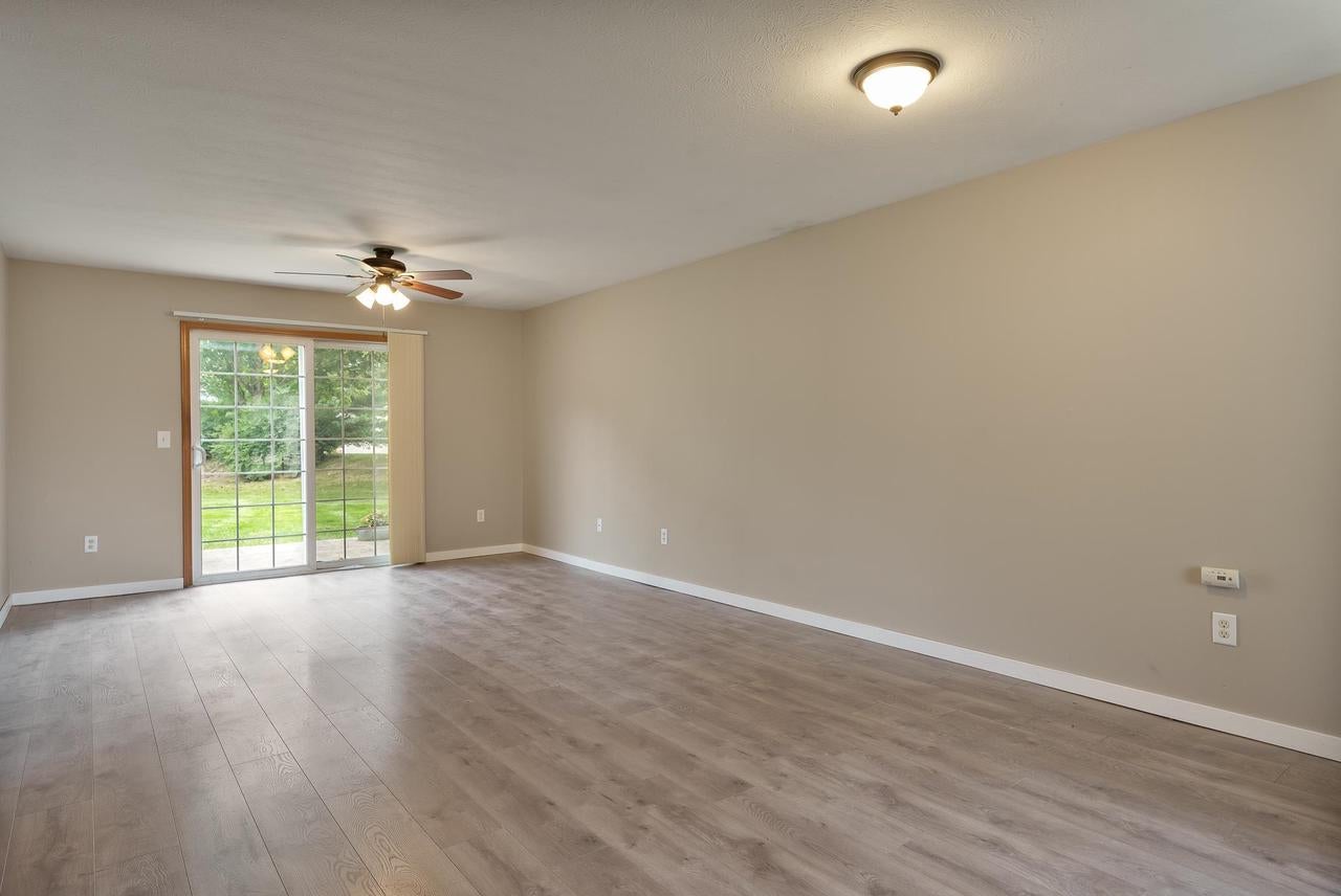Empty living room with gray wood-look floors, ceiling fan, and sliding glass door to the yard.