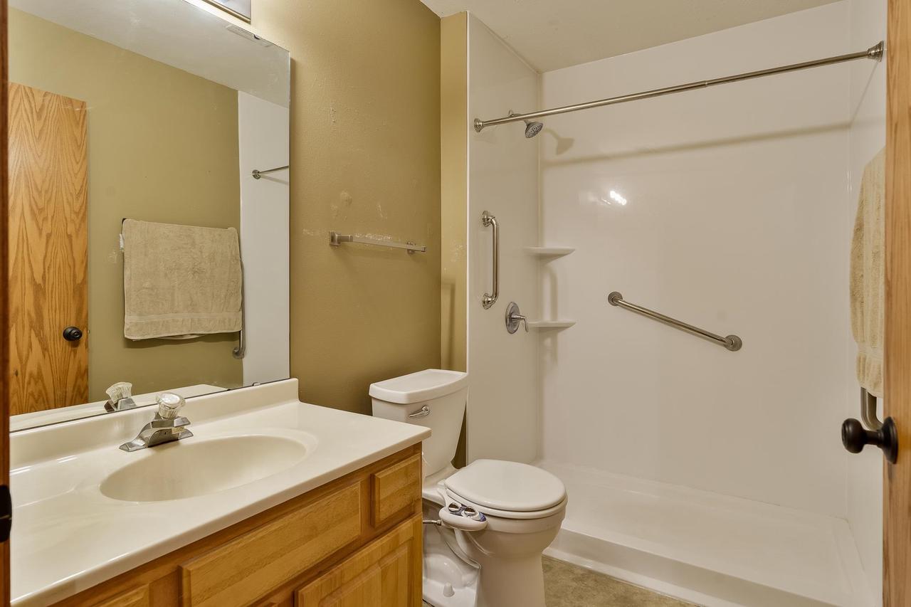Bathroom with an accessible white shower, grab bars, toilet, and wood vanity.