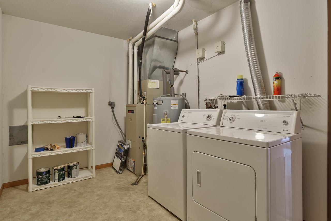 Laundry room with washer and dryer, furnace, exposed ductwork, and storage shelving.
