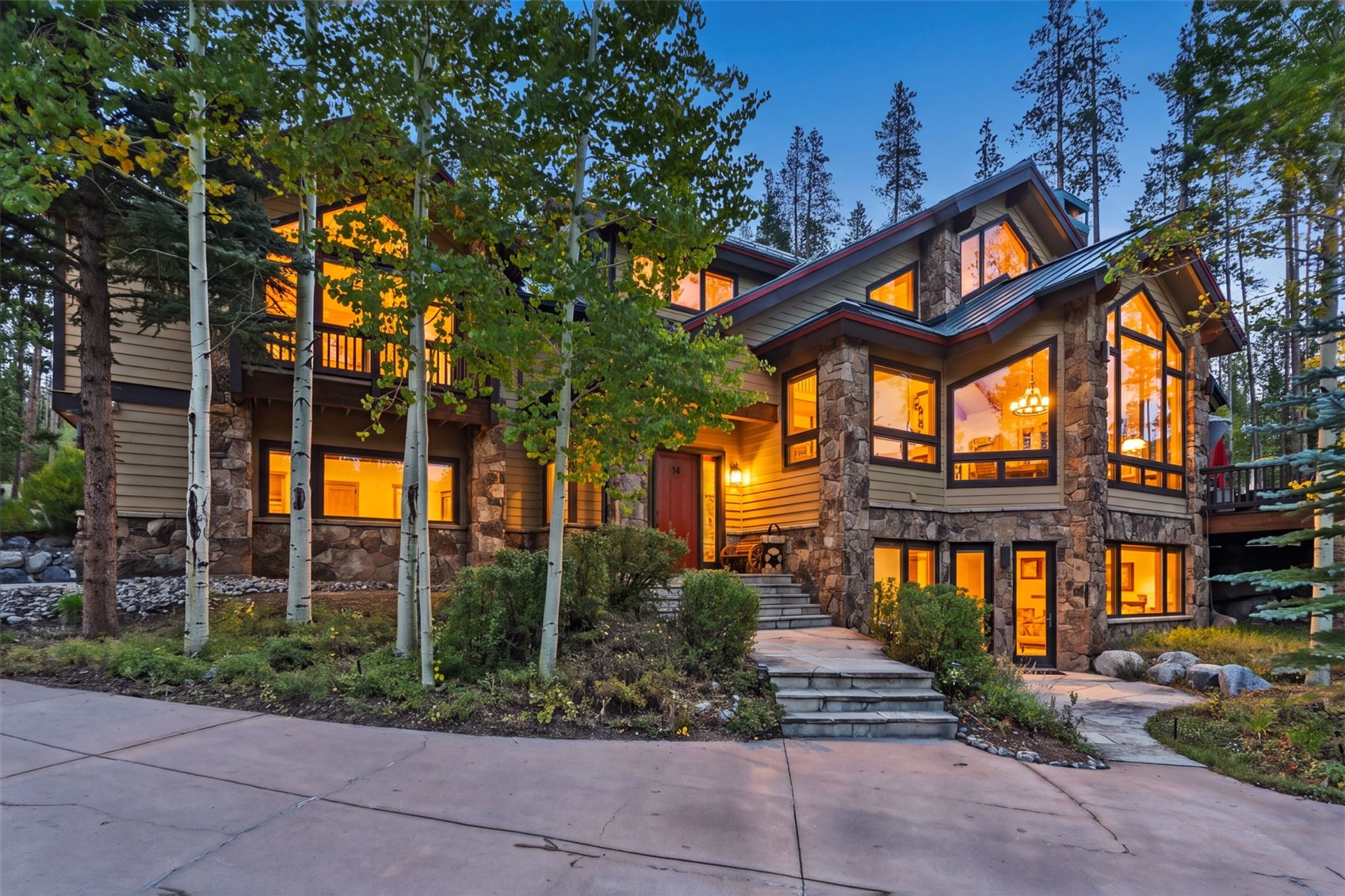 Mountain-style stone-and-siding home with illuminated windows, entry steps, and surrounding aspens at dusk.