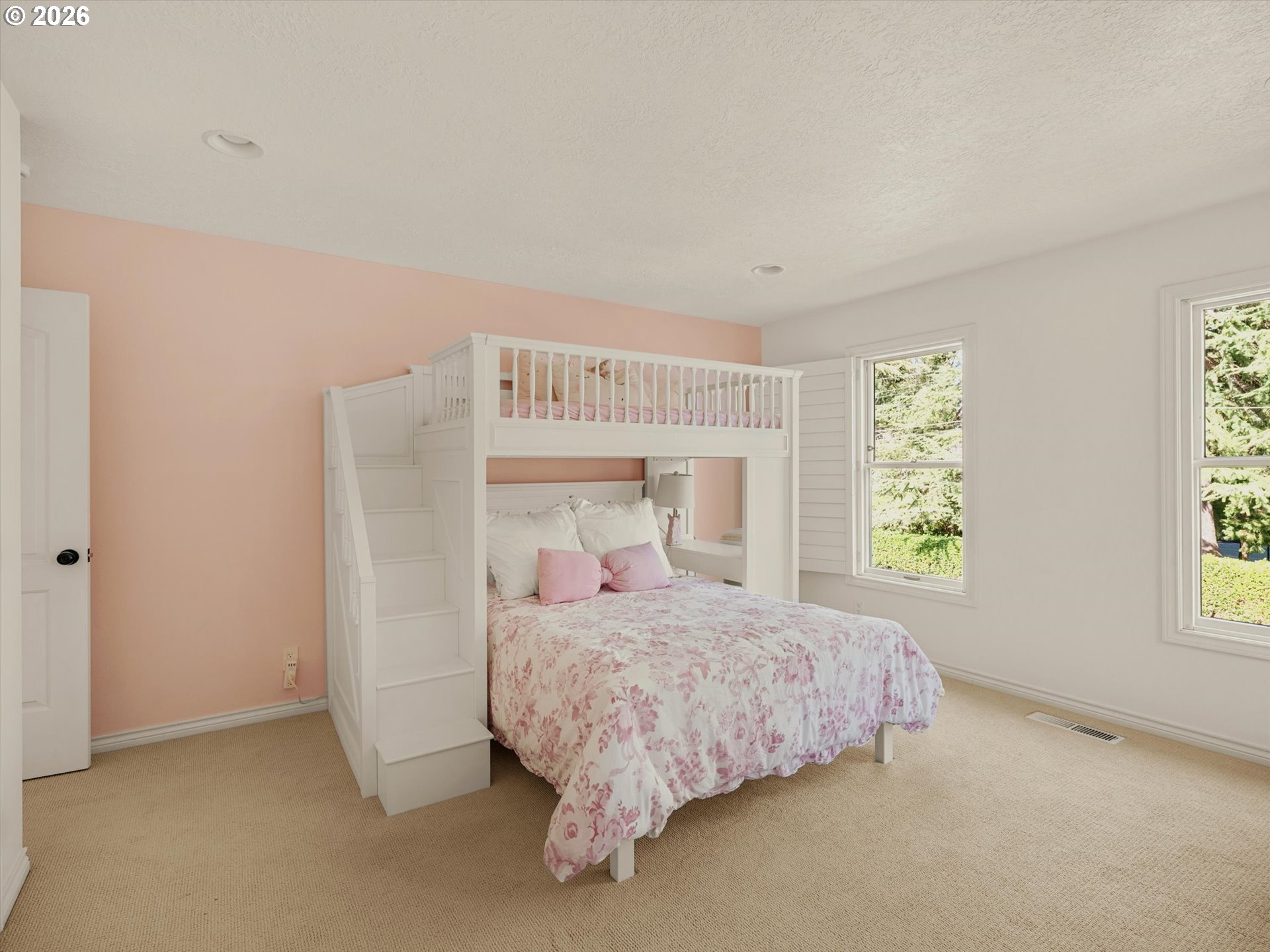 Bedroom with a white built-in bunk bed, pink floral bedding, and windows overlooking greenery.