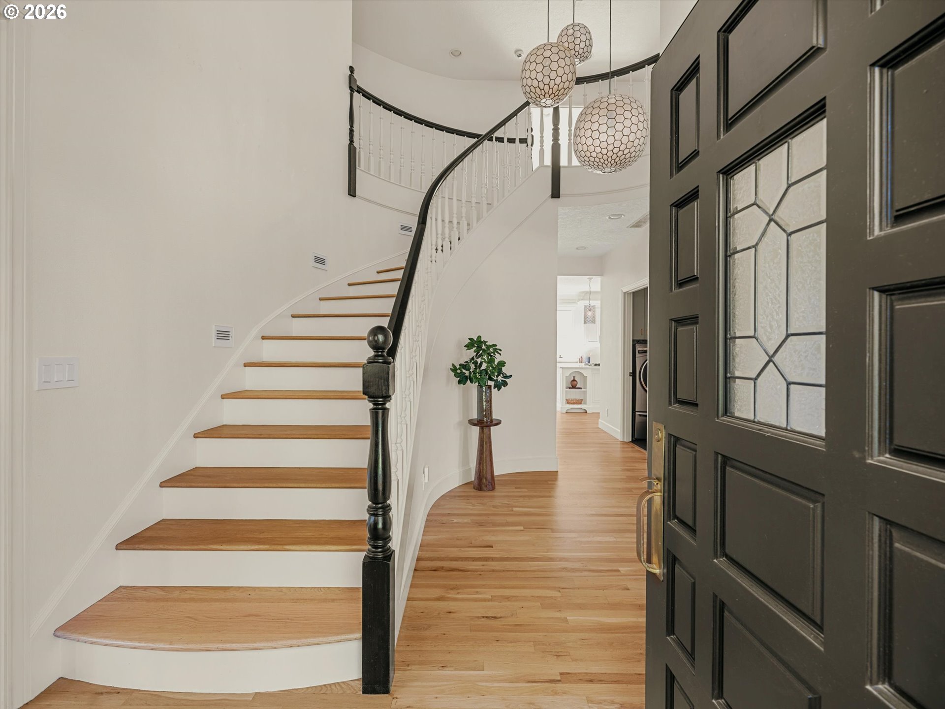 Entry foyer with a curved wood staircase, dark glass-paneled front door, and three pendant lights.