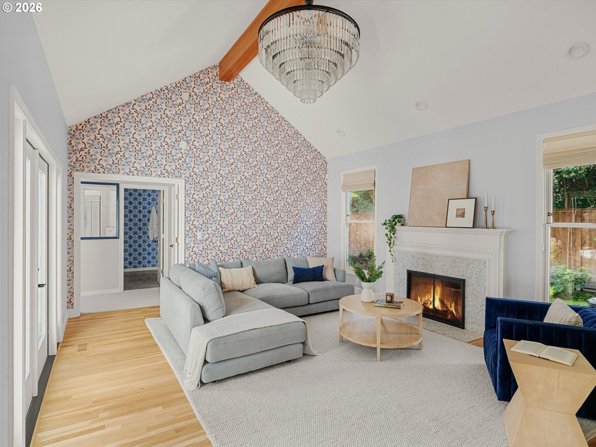 Living room with a vaulted ceiling, floral wallpaper accent wall, gray sectional, and lit fireplace.