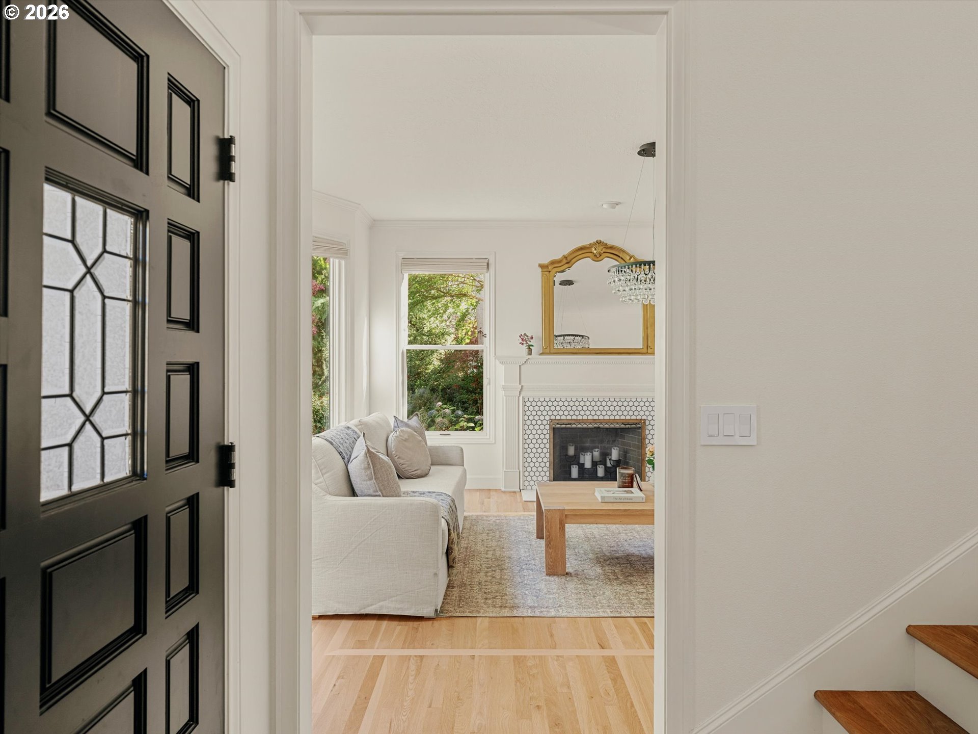 Living room with a white sofa, tiled fireplace, gold-framed mirror, and hardwood floors, viewed through the entry doorway.
