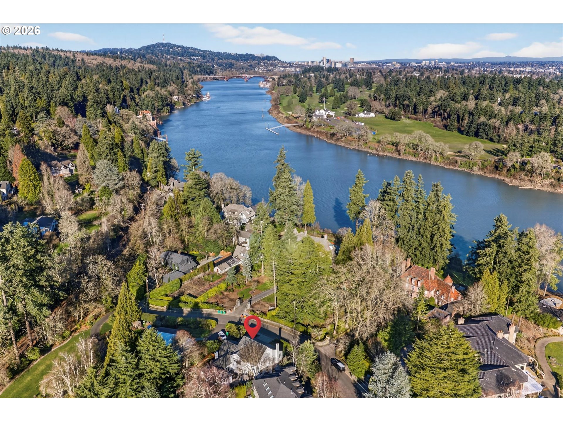 Aerial view of the marked property near a wooded riverbank and surrounding homes.