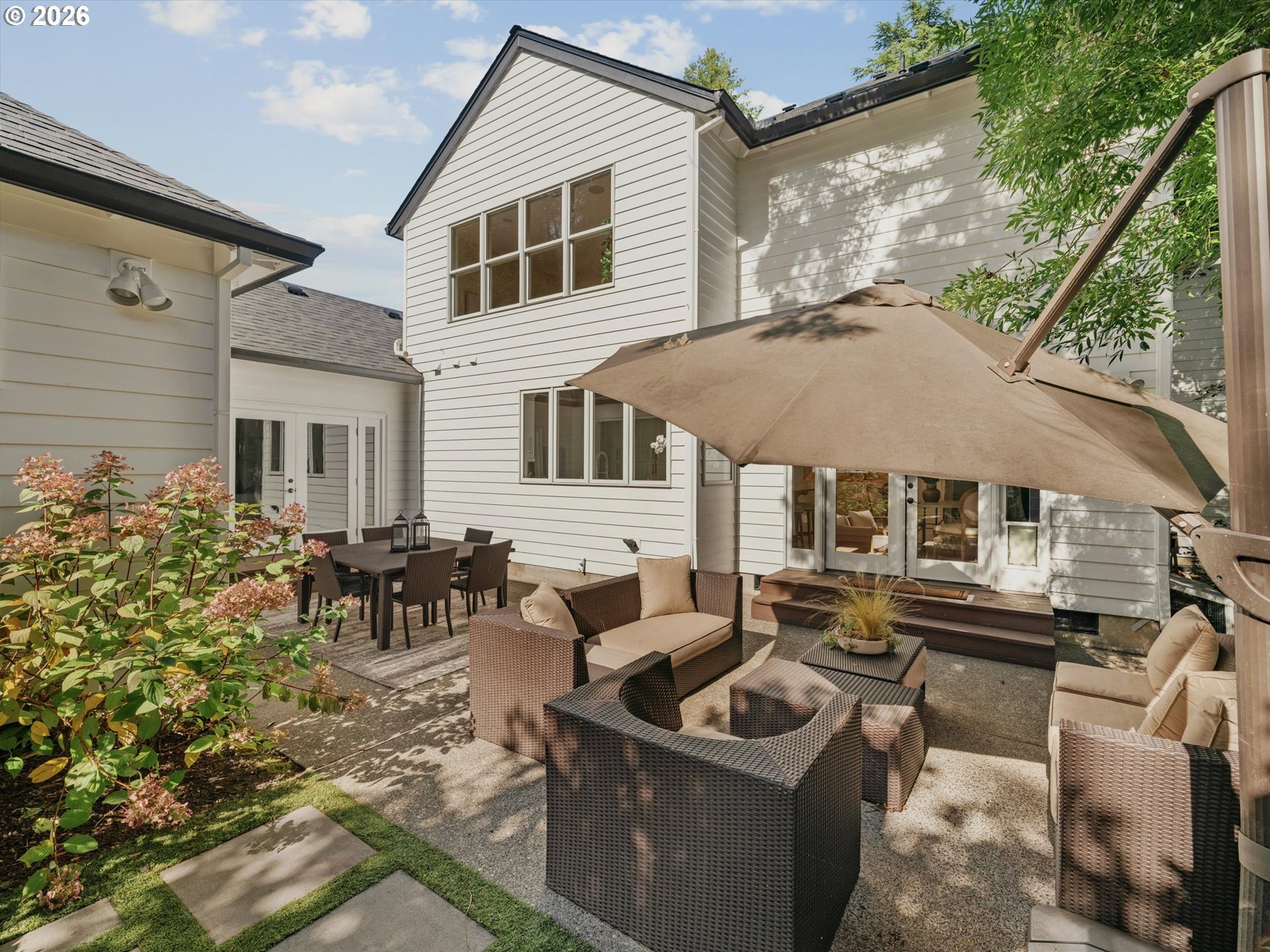 Furnished patio with wicker seating and dining area beneath a large umbrella behind a white house.