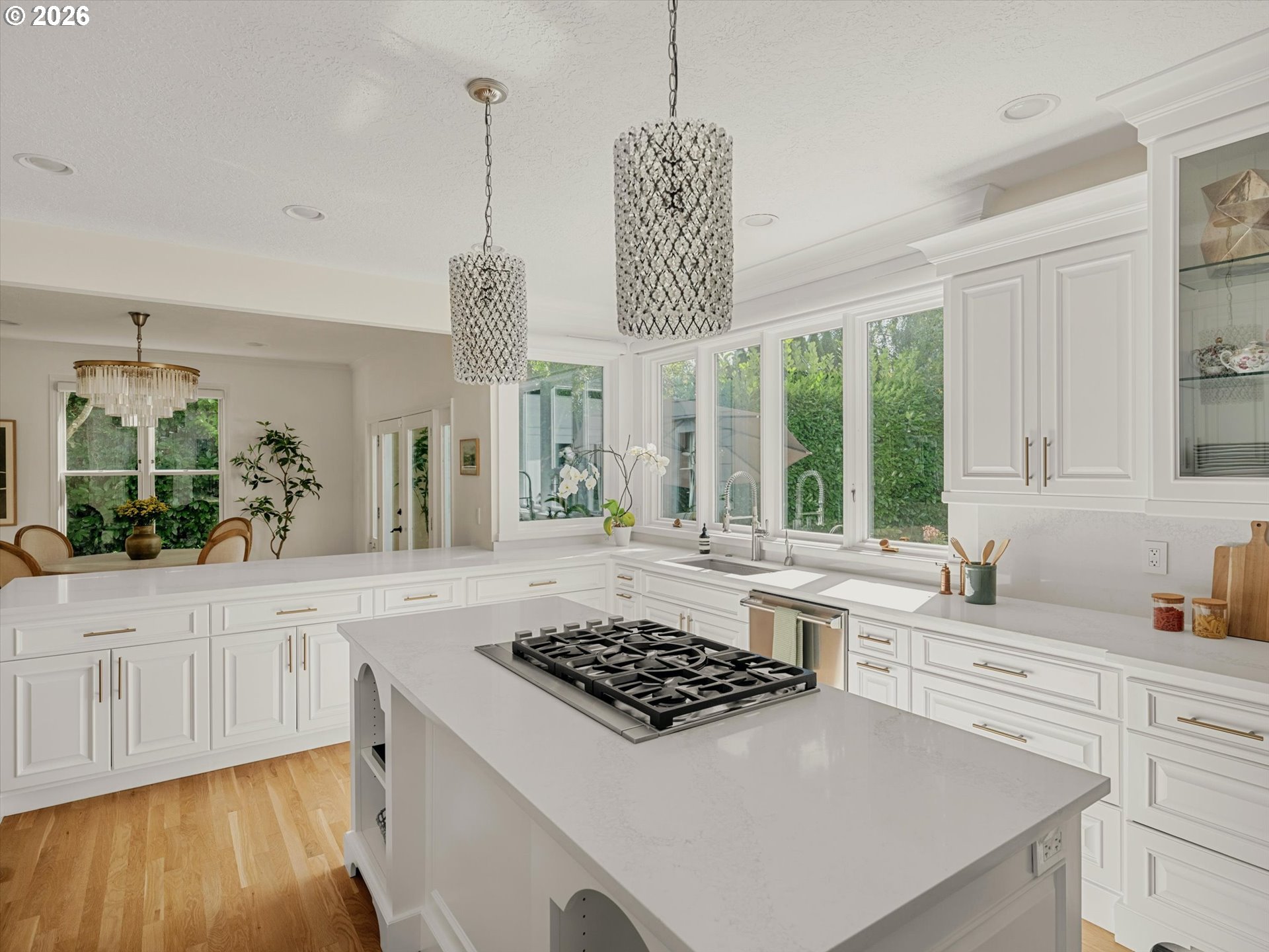 White kitchen with a large cooktop island, wide windows, and crystal pendant lights.