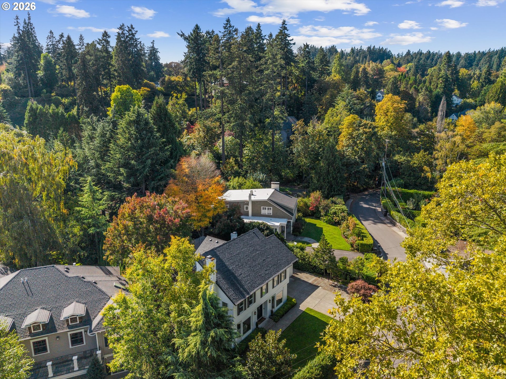 Aerial view of a home surrounded by dense trees, neighboring houses, and autumn foliage.