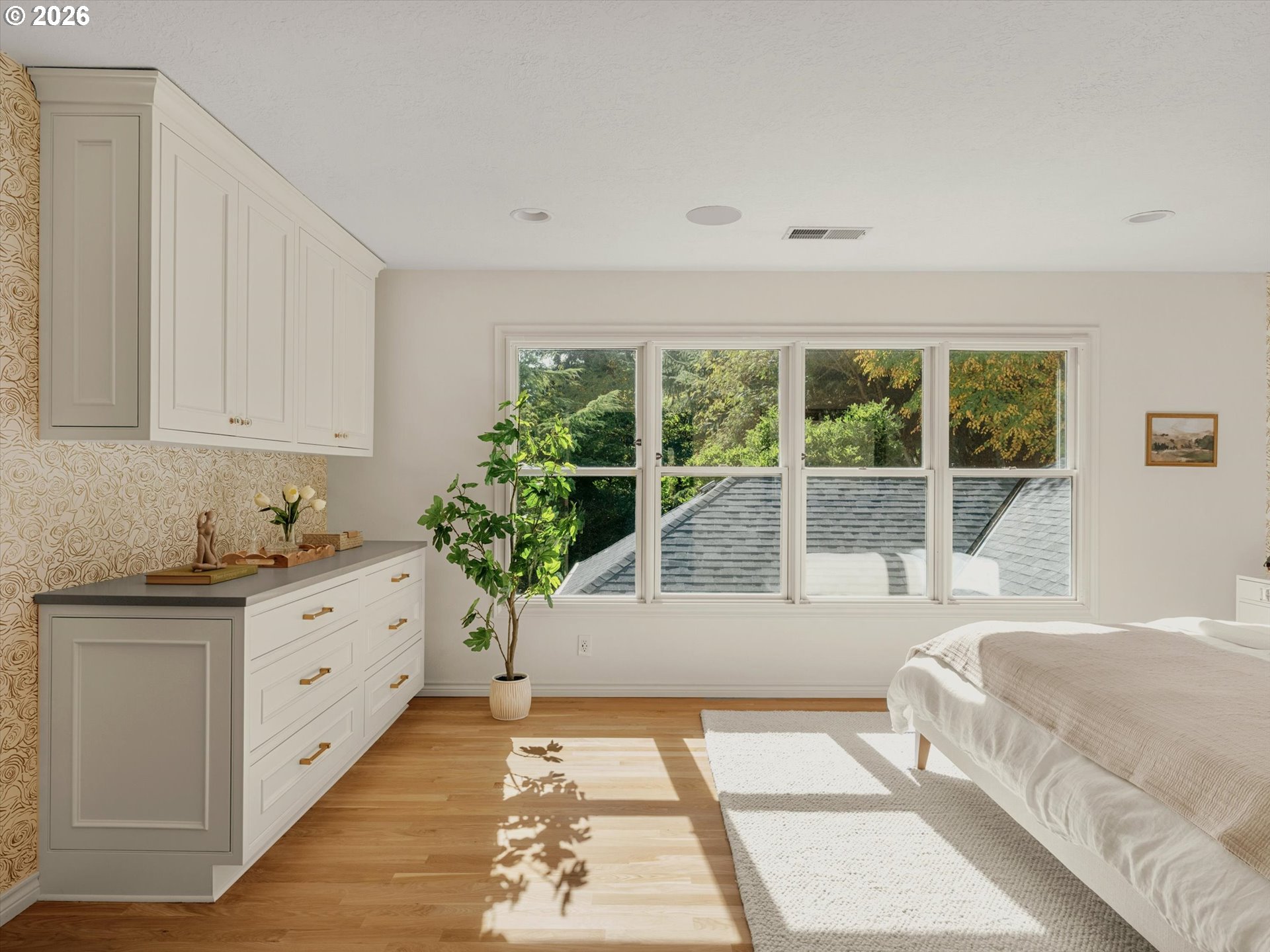 Bright bedroom with built-in white cabinetry and large windows overlooking leafy trees.