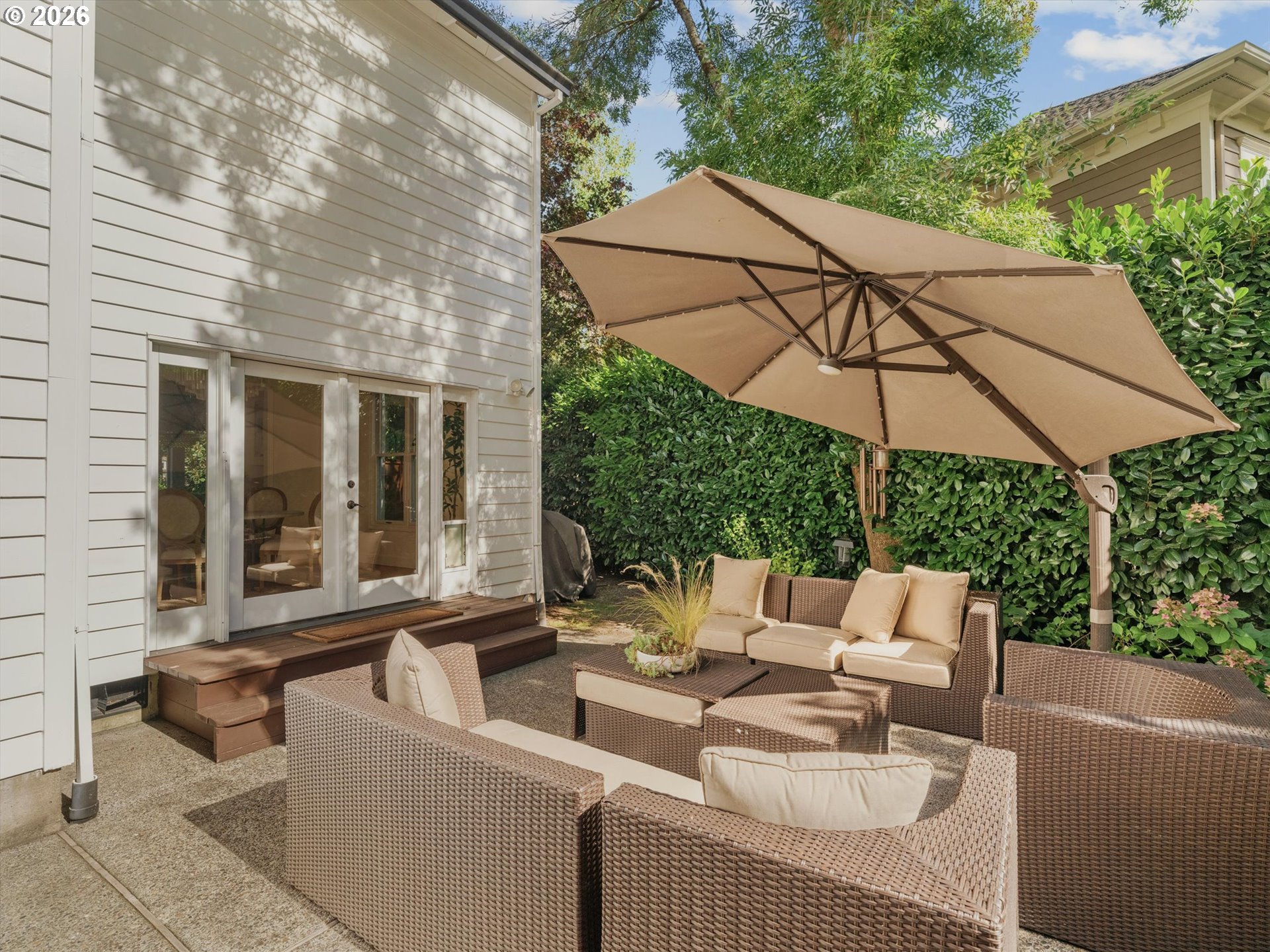Backyard patio with wicker seating and a large umbrella beside sliding glass doors.