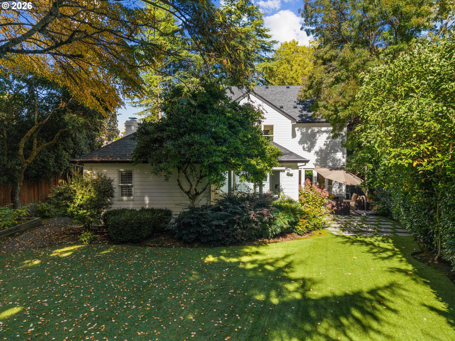 White-sided house behind a broad lawn and mature trees, with a stepping-stone path to the patio.