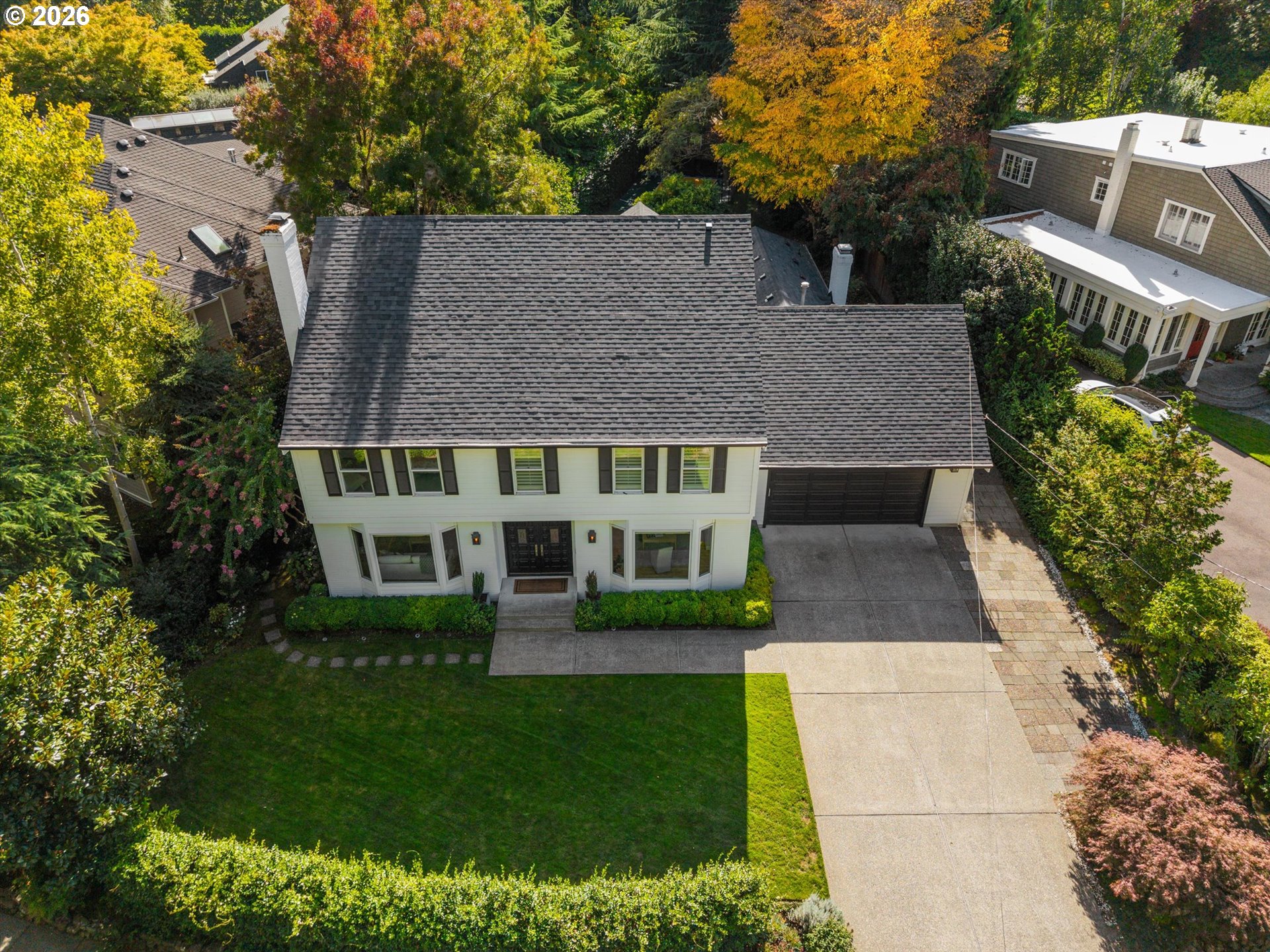 Aerial view of a two-story white house with an attached garage and tree-lined lawn.
