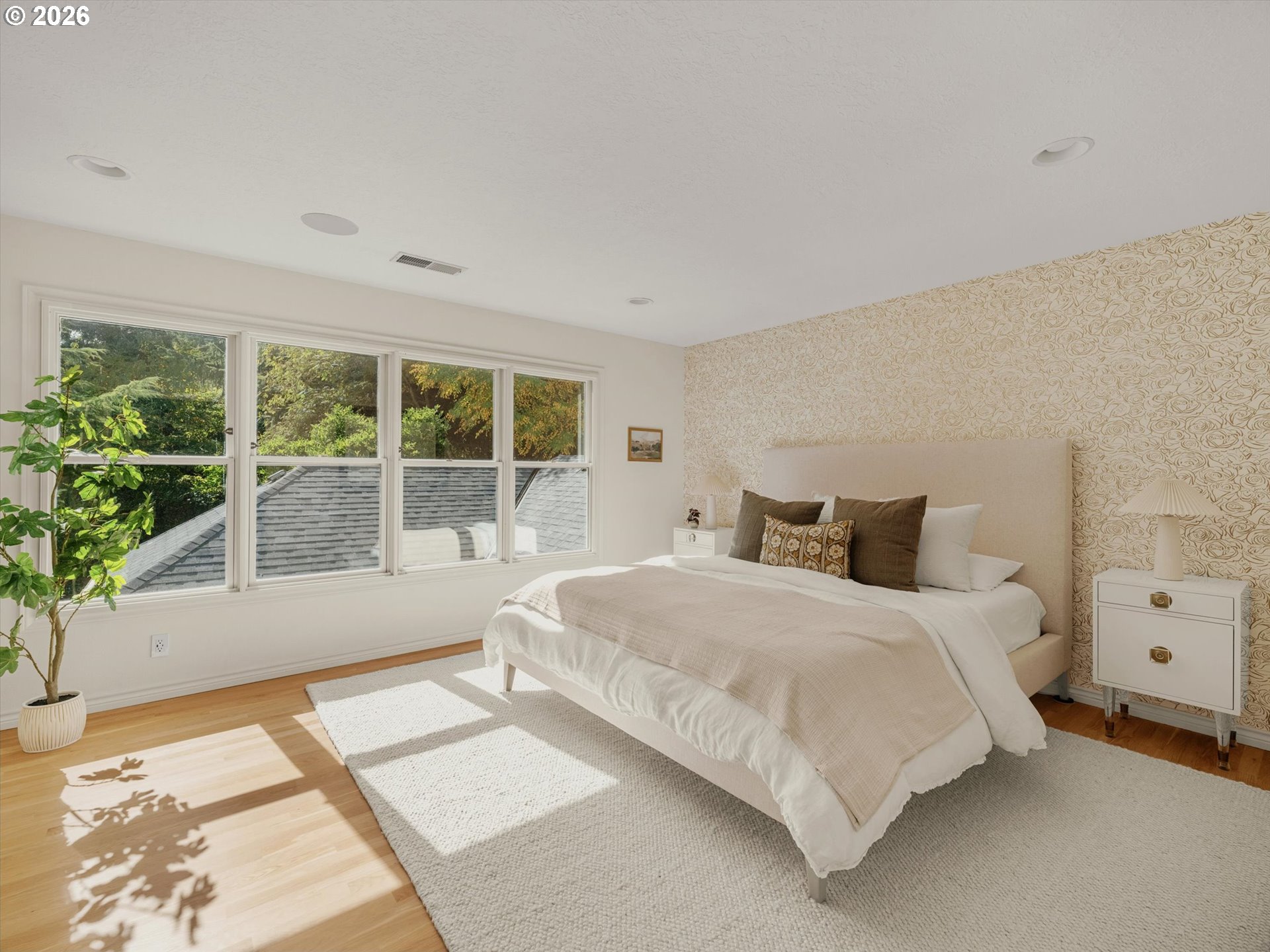 Bright bedroom with an upholstered bed, patterned accent wall, and wide windows overlooking trees.