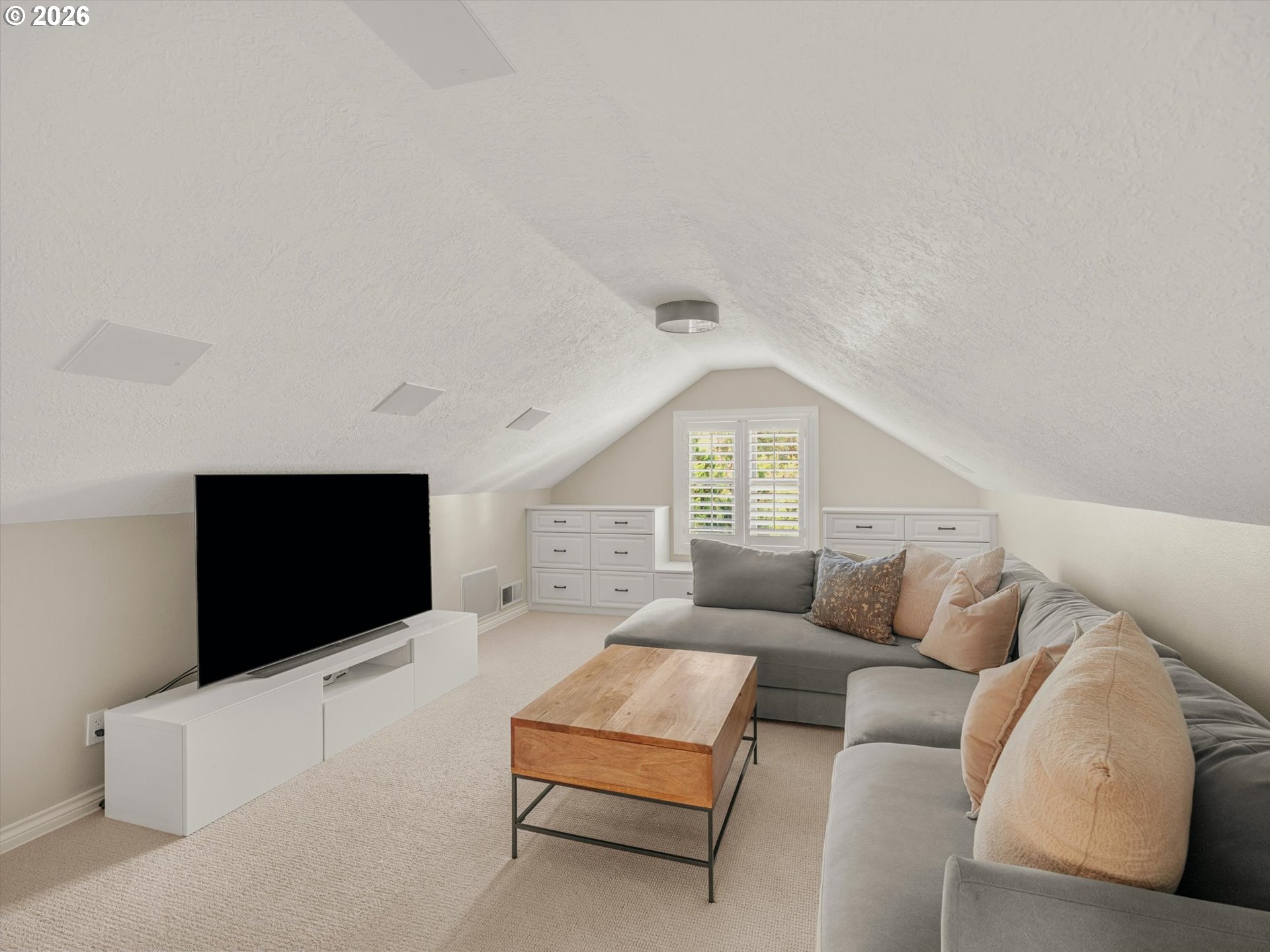 Upstairs media room with a gray sectional, wooden coffee table, television, and built-in drawers.