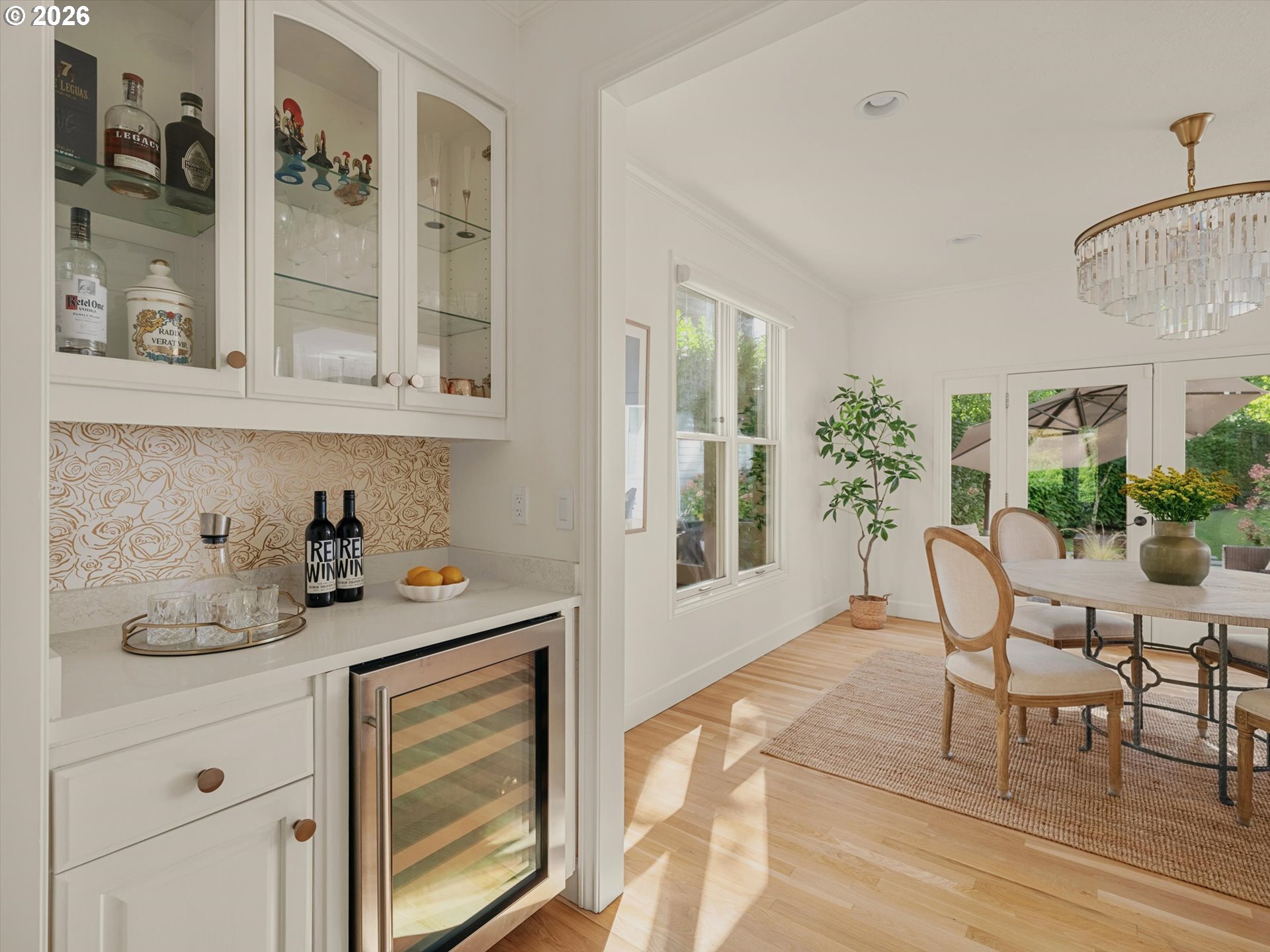 Dining room with a built-in bar, glass-front cabinets, crystal chandelier, and garden-facing French doors.