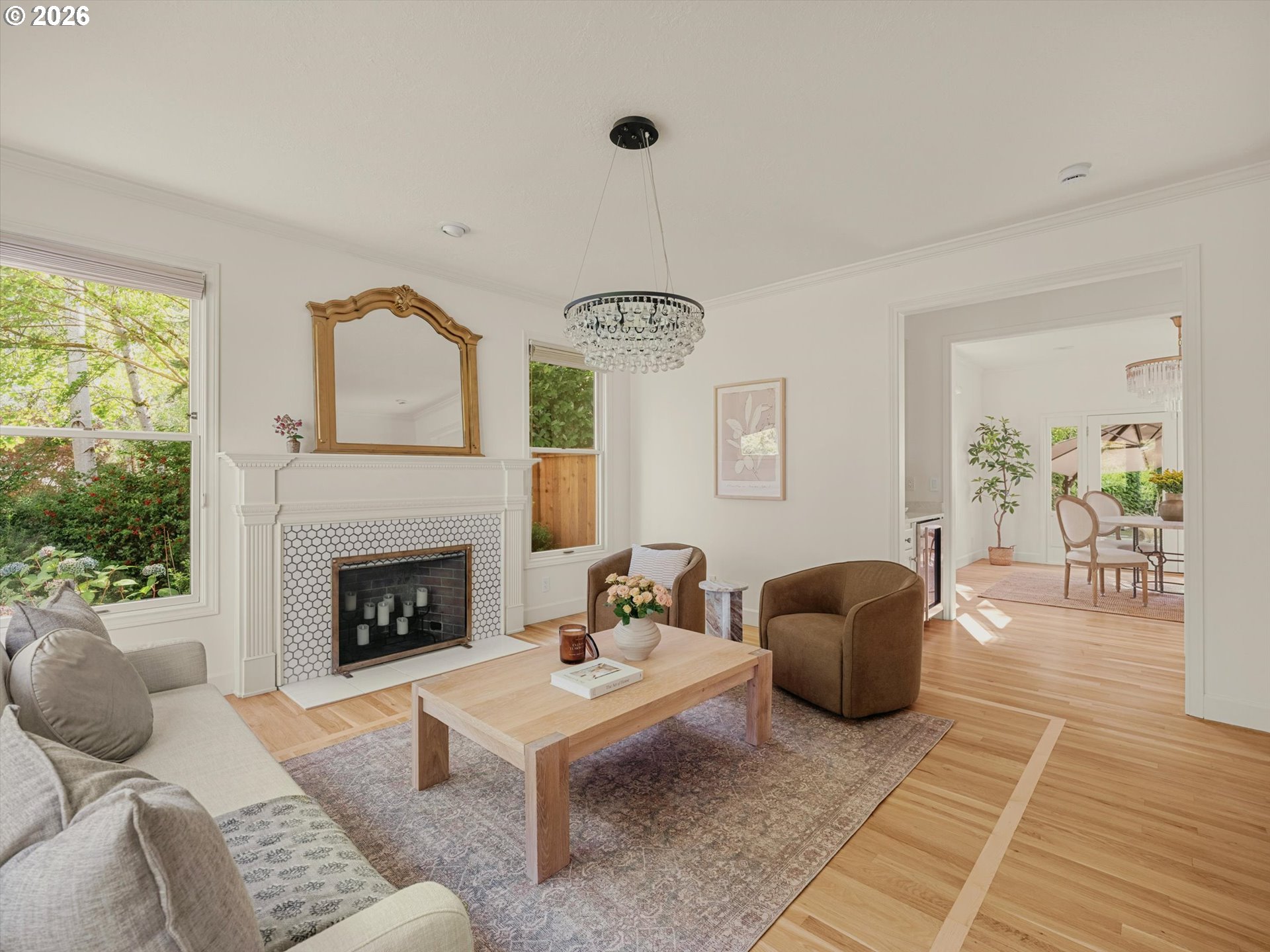 Staged living room with a tiled fireplace and crystal chandelier, opening into a bright dining room.
