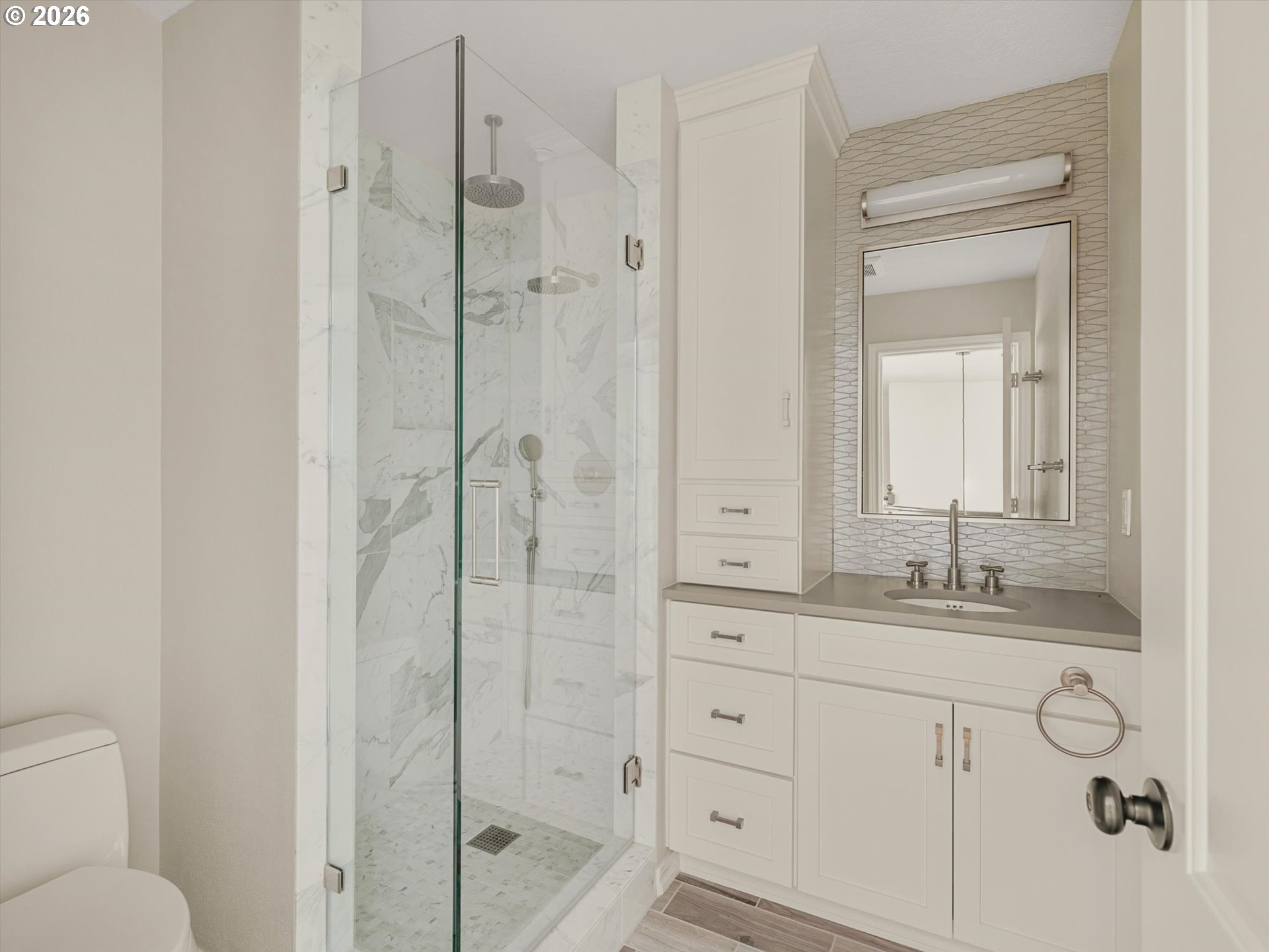 Bathroom with a marble walk-in shower, white cabinetry, and a geometric tile backsplash.