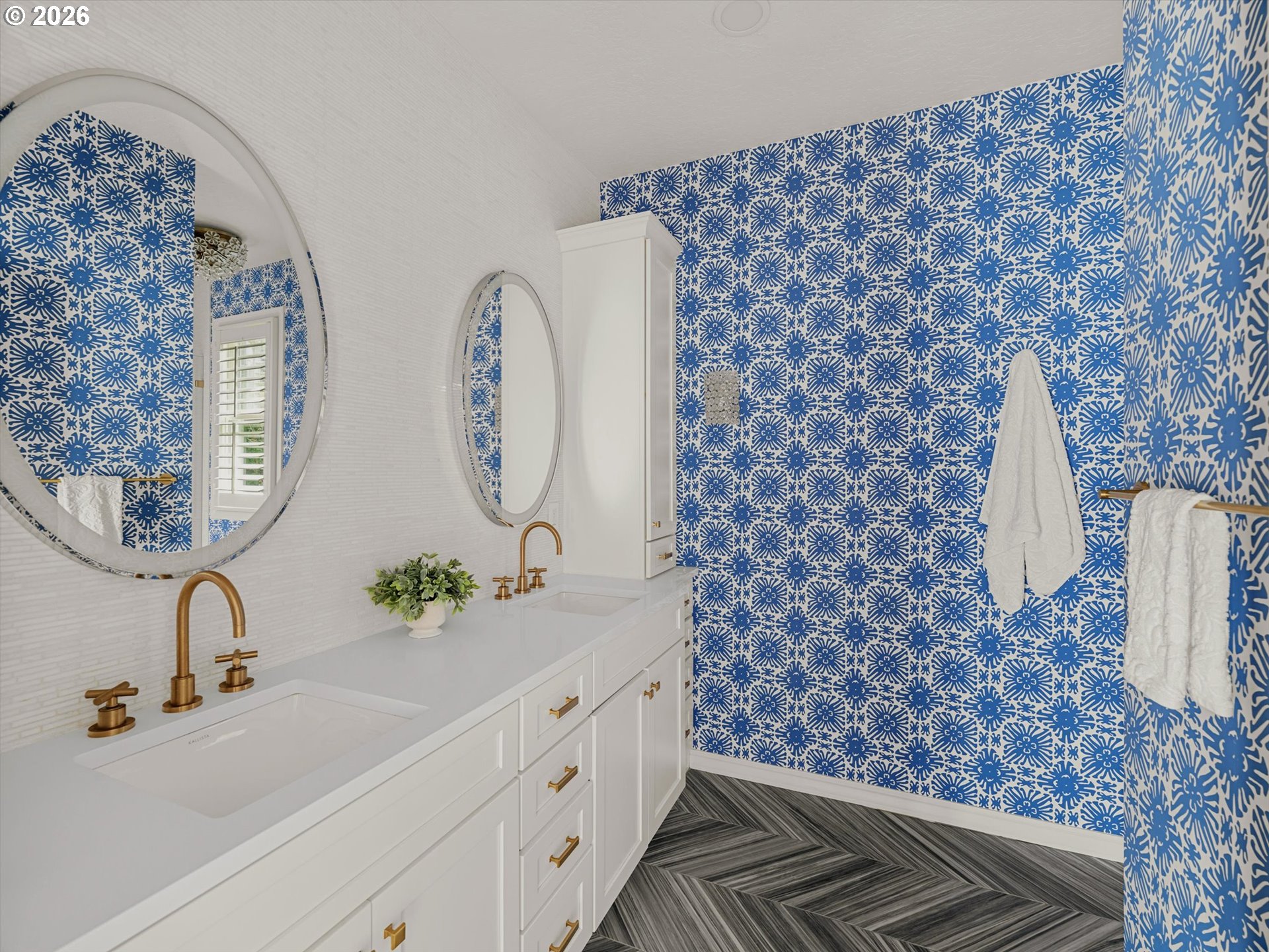 Bathroom with a white double vanity, brass faucets, and blue-and-white floral wallpaper.