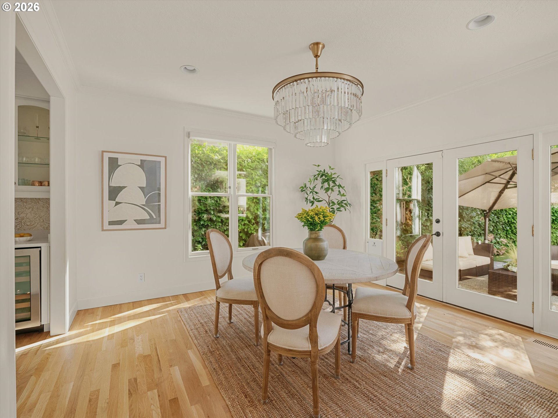 Dining room with a crystal chandelier, round table, hardwood floors, and French doors to a leafy patio.