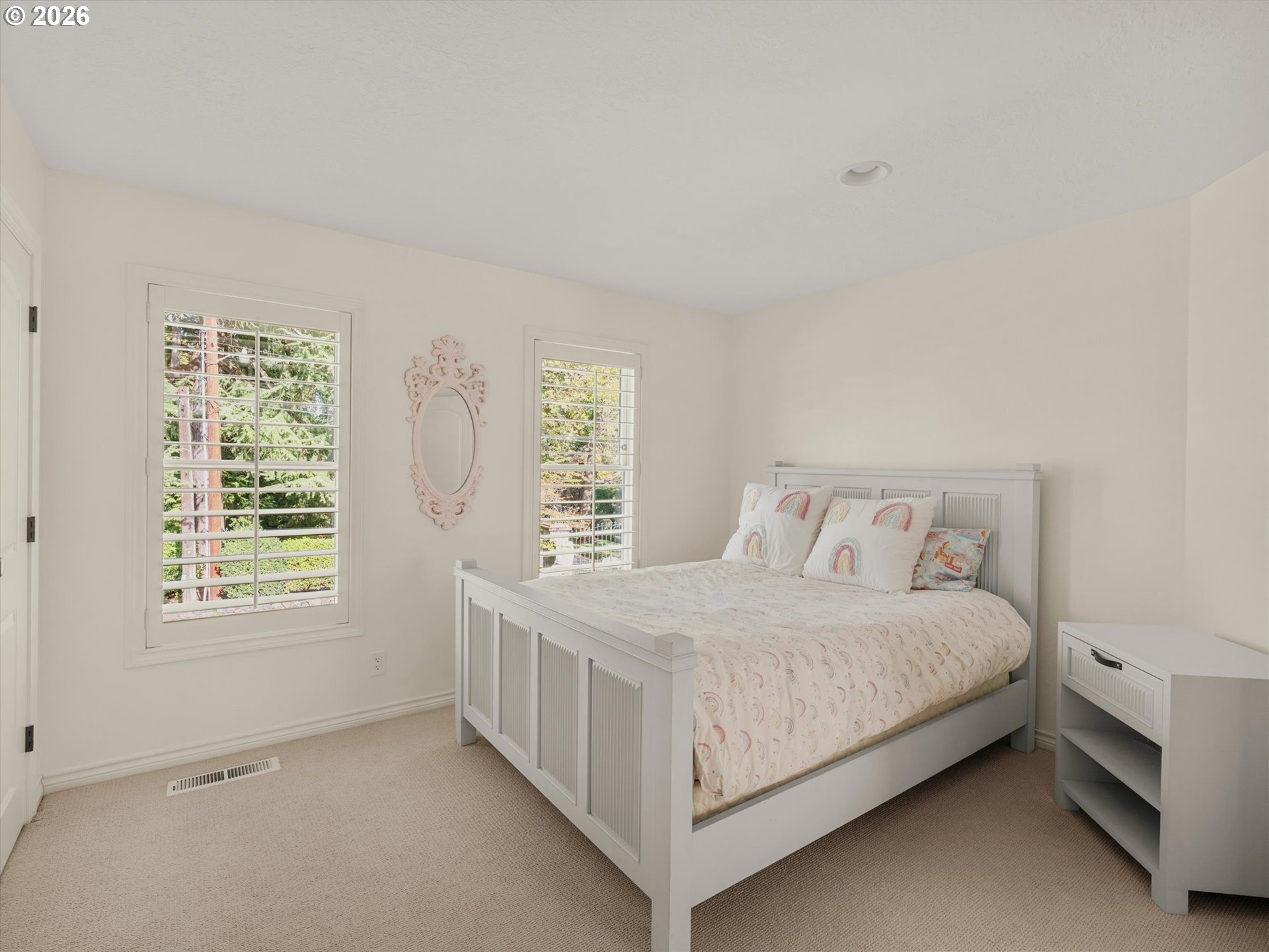 Bedroom with a white bed, pale patterned bedding, and two shuttered windows.