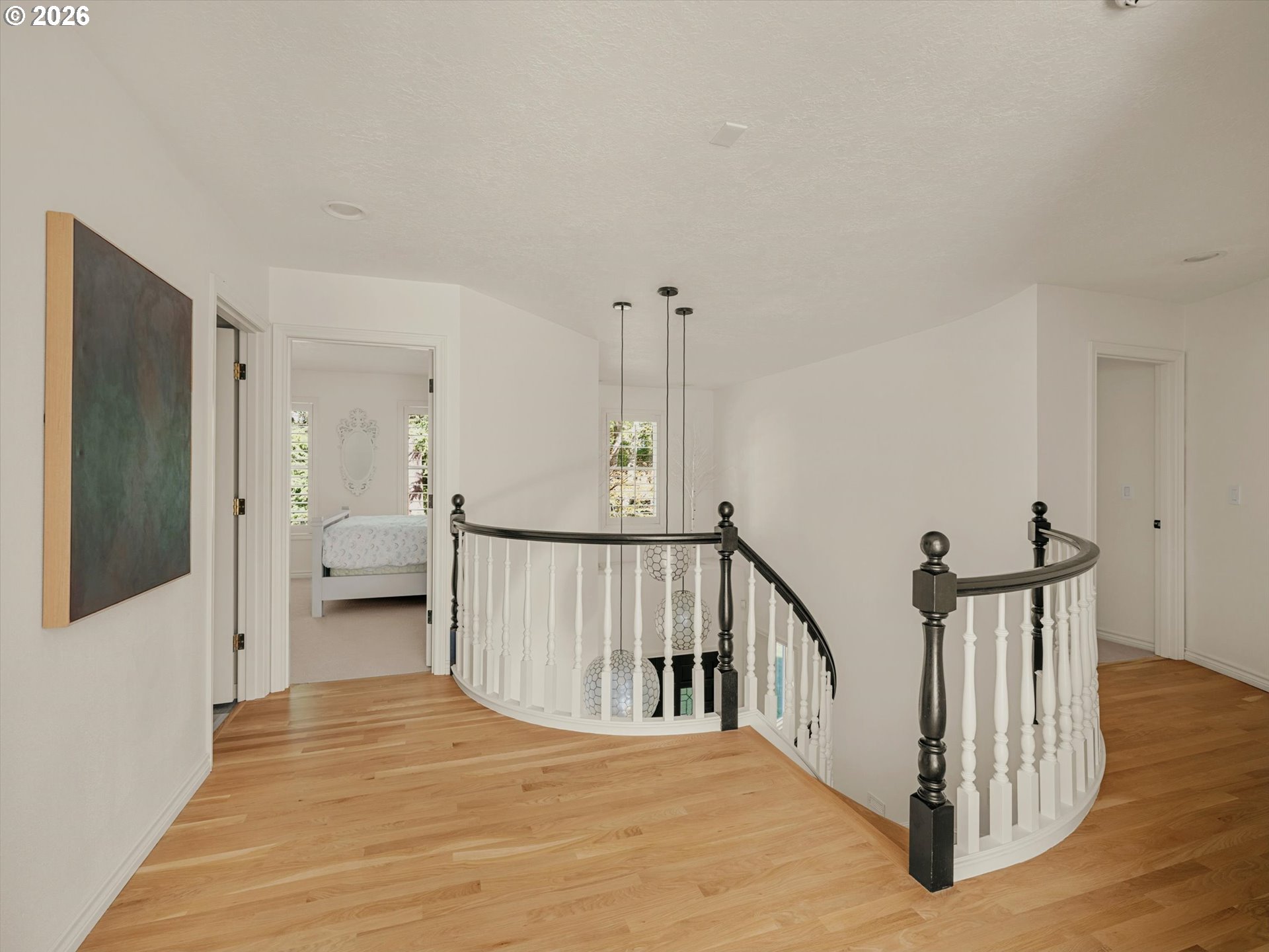 Upstairs landing with curved staircase railing, hardwood floors, and a bedroom visible through the doorway.