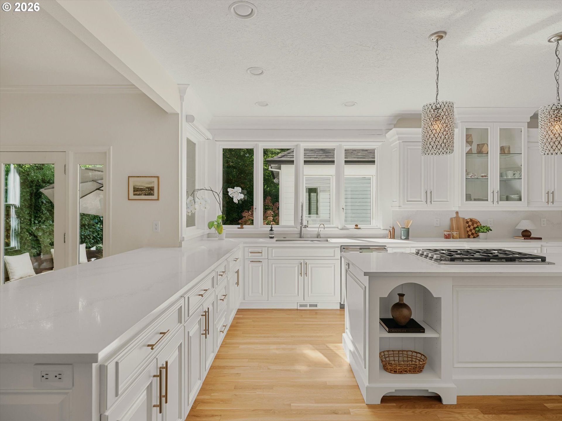 Bright white kitchen with a large island, quartz counters, brass hardware, and windows overlooking greenery.