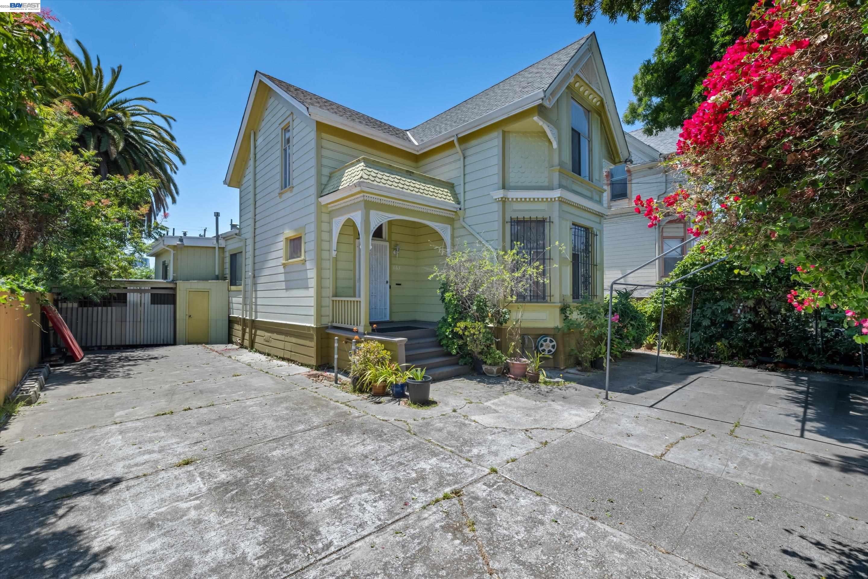 Pale green Victorian house with a covered porch, driveway, and flowering bougainvillea.