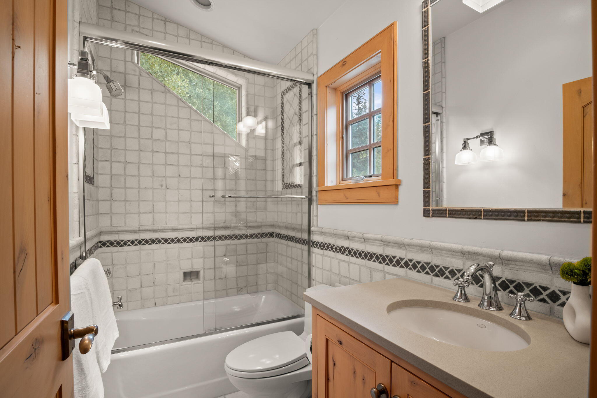 Bathroom with tiled glass-enclosed tub and shower, wood vanity, and sunlit window.