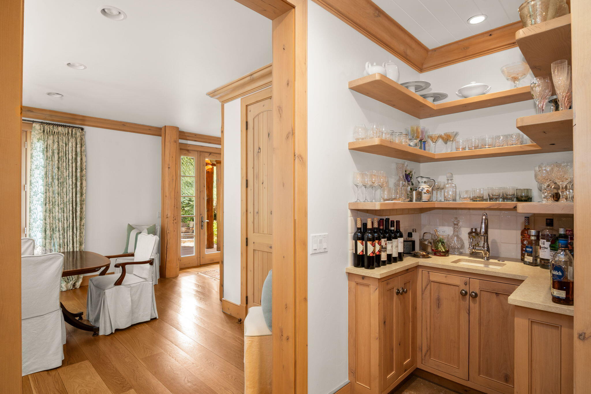 Wood-paneled wet bar with glassware and sink beside a dining nook with glass doors.