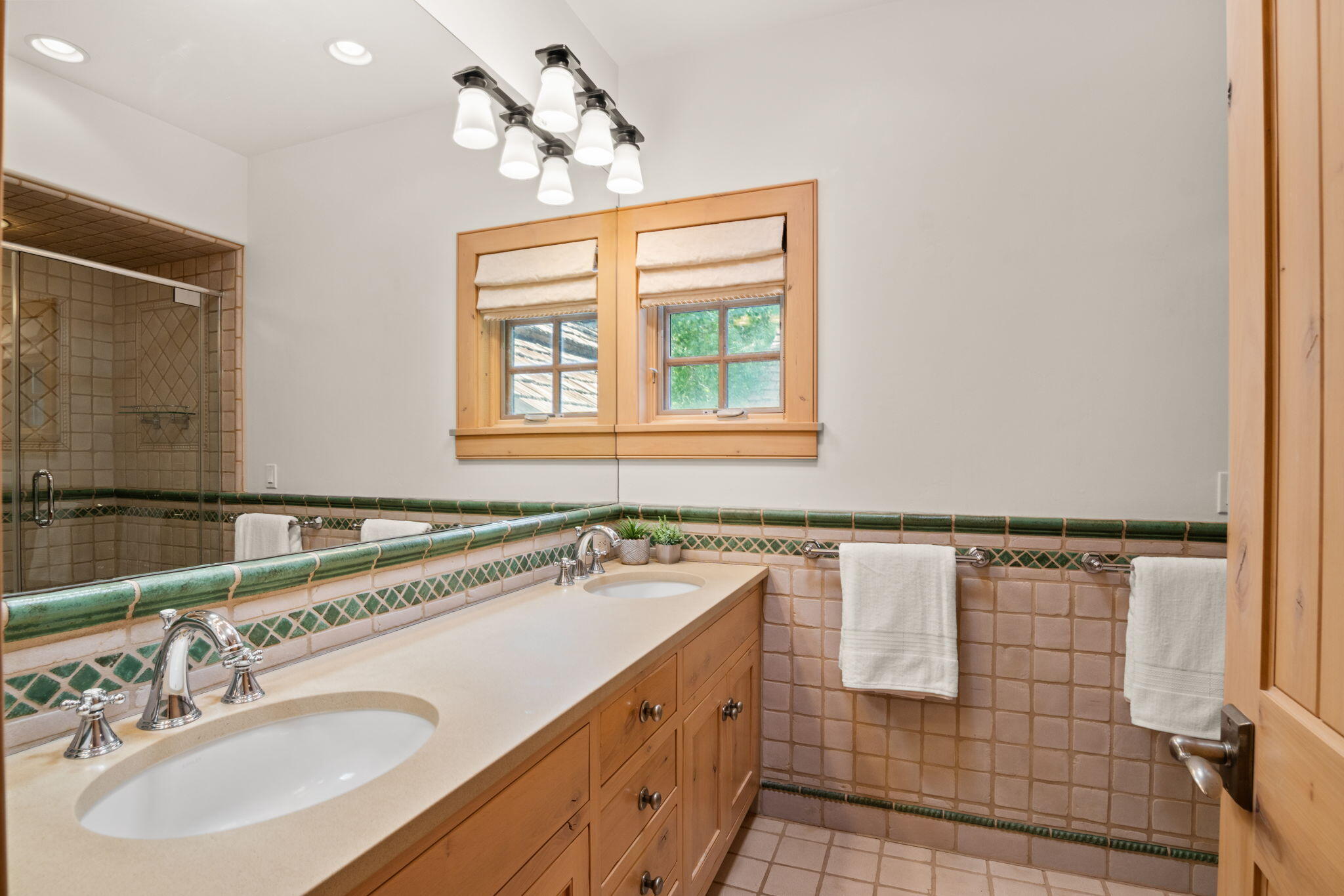 Bathroom with a double-sink wood vanity, green tile accents, and a glass-enclosed shower.