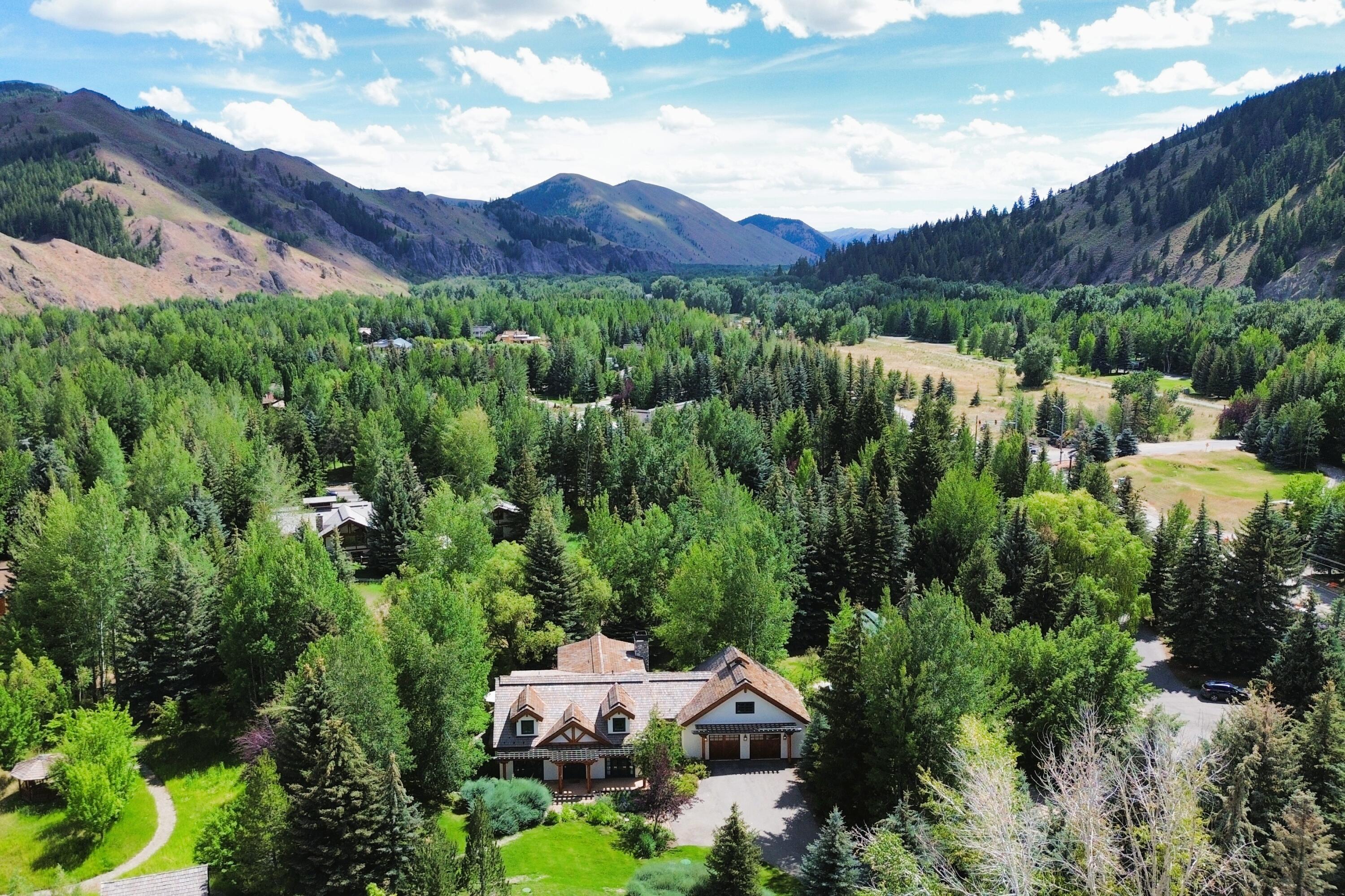 Aerial view of a large house surrounded by trees, with mountain ridges beyond.