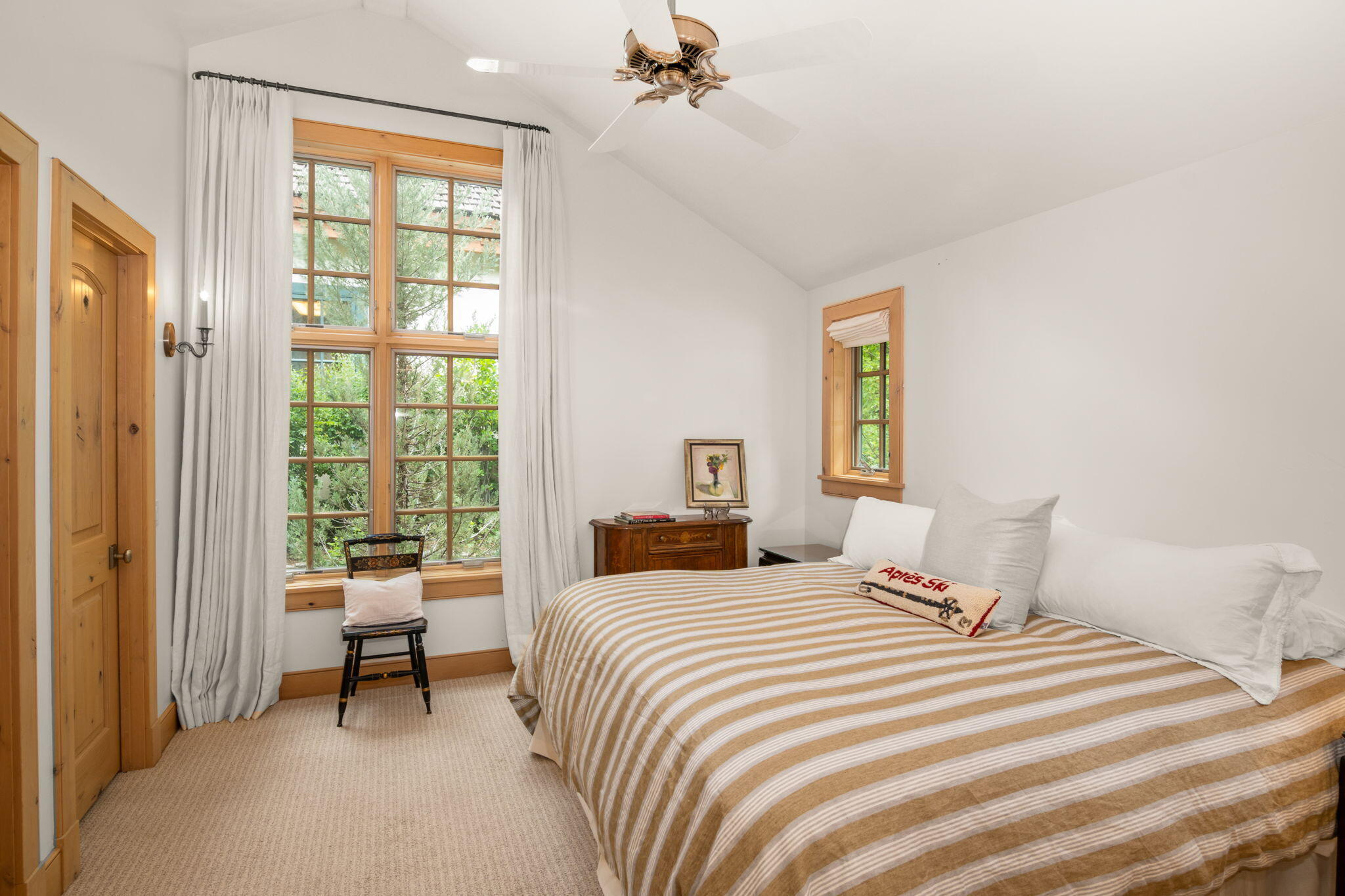 Bedroom with a striped bed, tall wood-framed windows, and a vaulted ceiling.